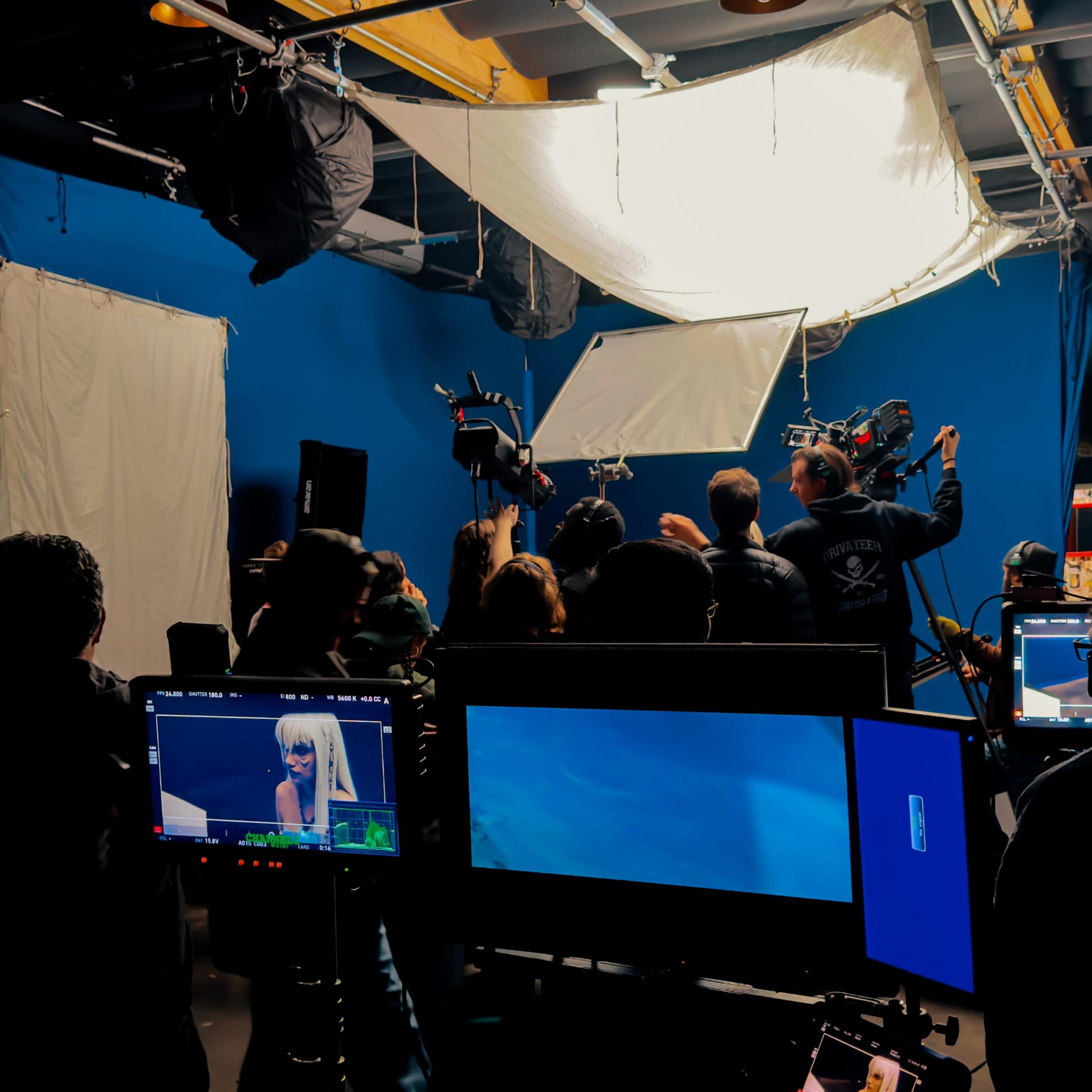 A film crew is seen working in a studio with blue walls, multiple cameras, and lights set up for a shoot.