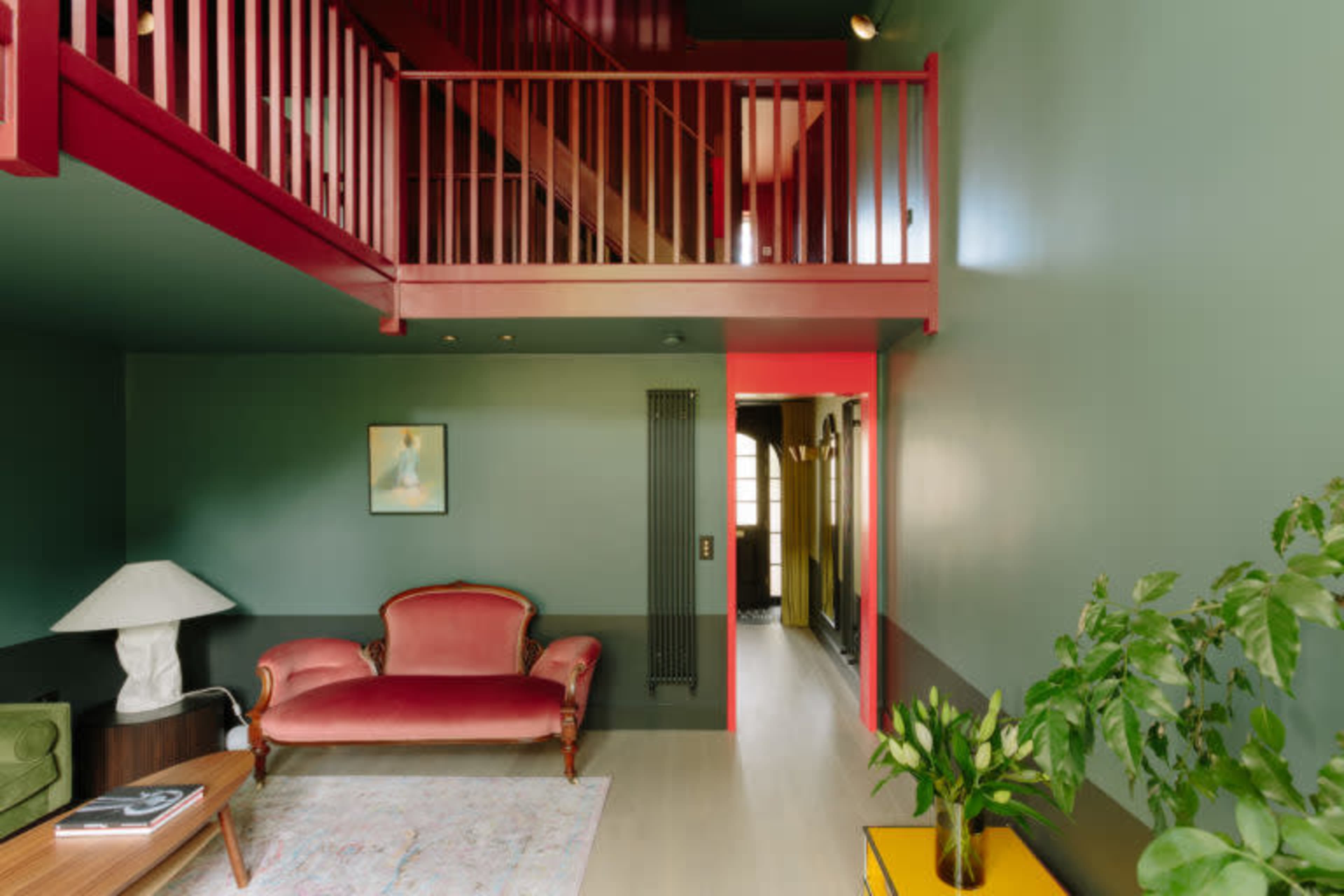 A modern living room with green walls, a red balcony, a vintage-style sofa, a floor lamp, and potted plants.
