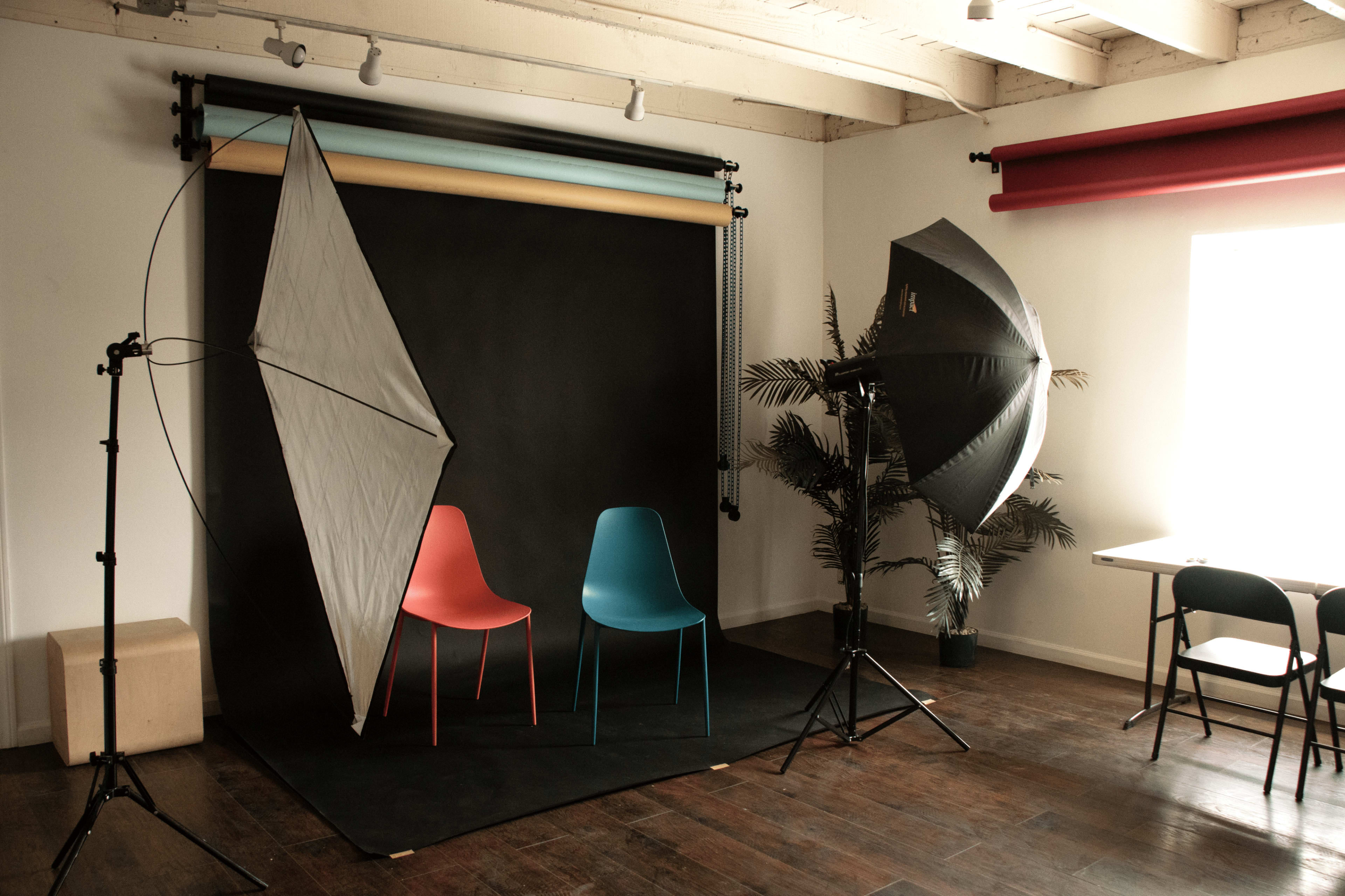 A photography studio setup with two chairs, a black backdrop, and various lighting equipment.