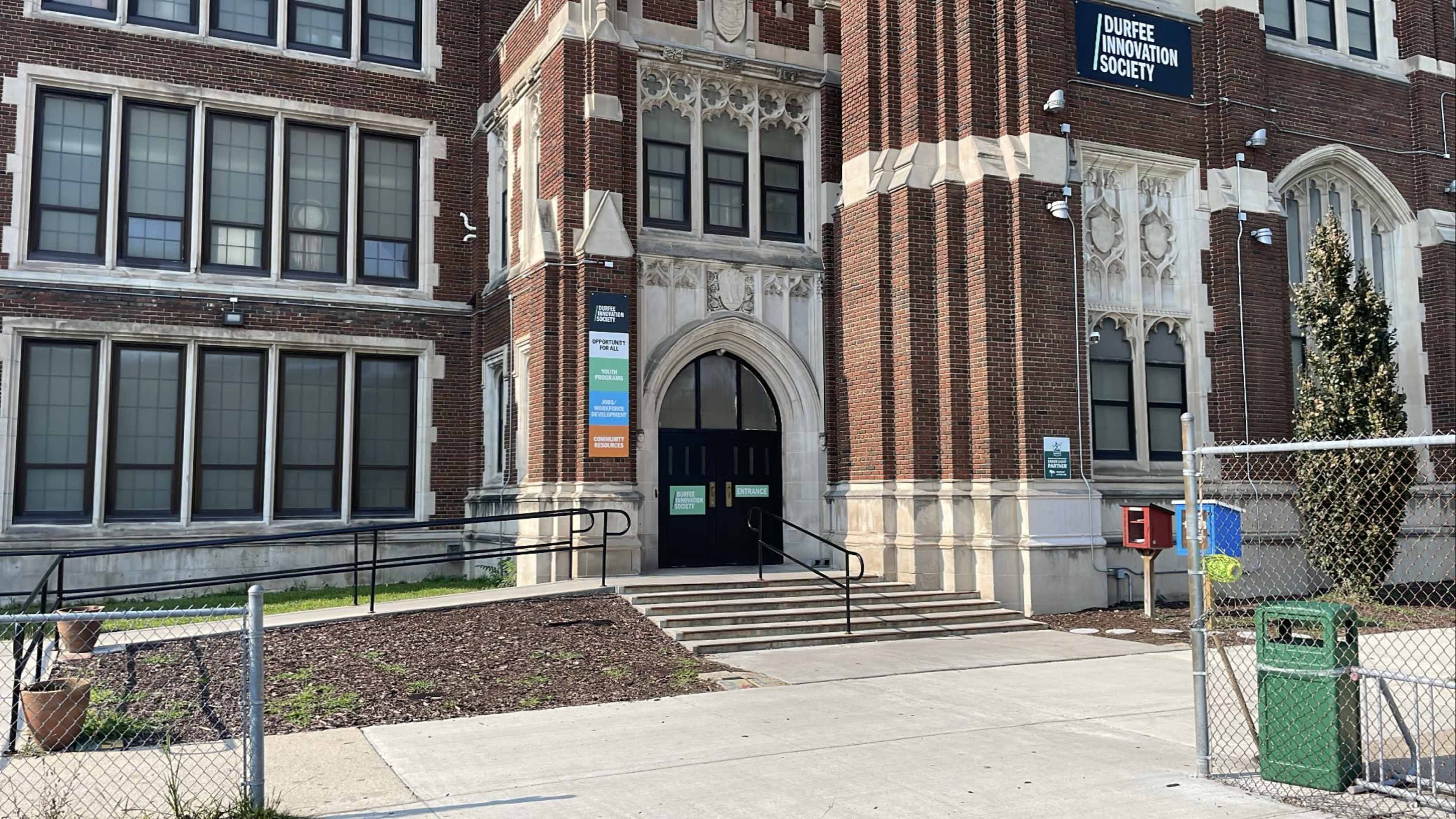 The entrance of a brick school building with a ramp and several windows.