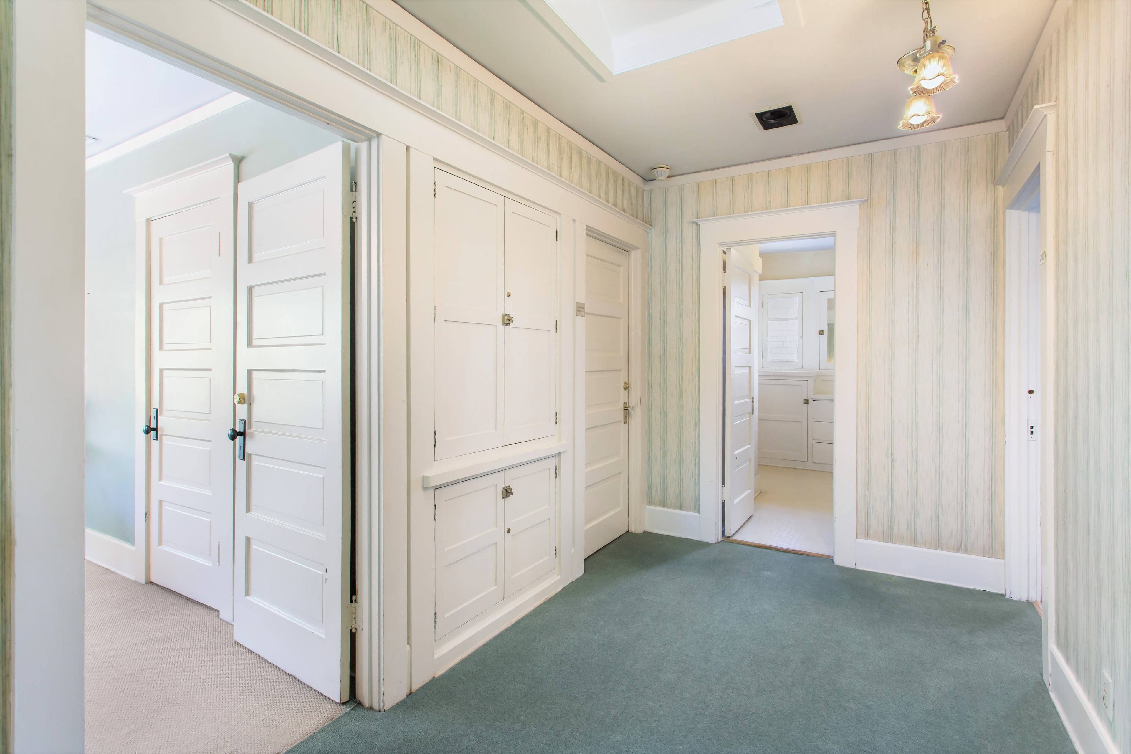 The image shows a hallway with light green carpet, featuring several white doors and walls with a striped wallpaper pattern.