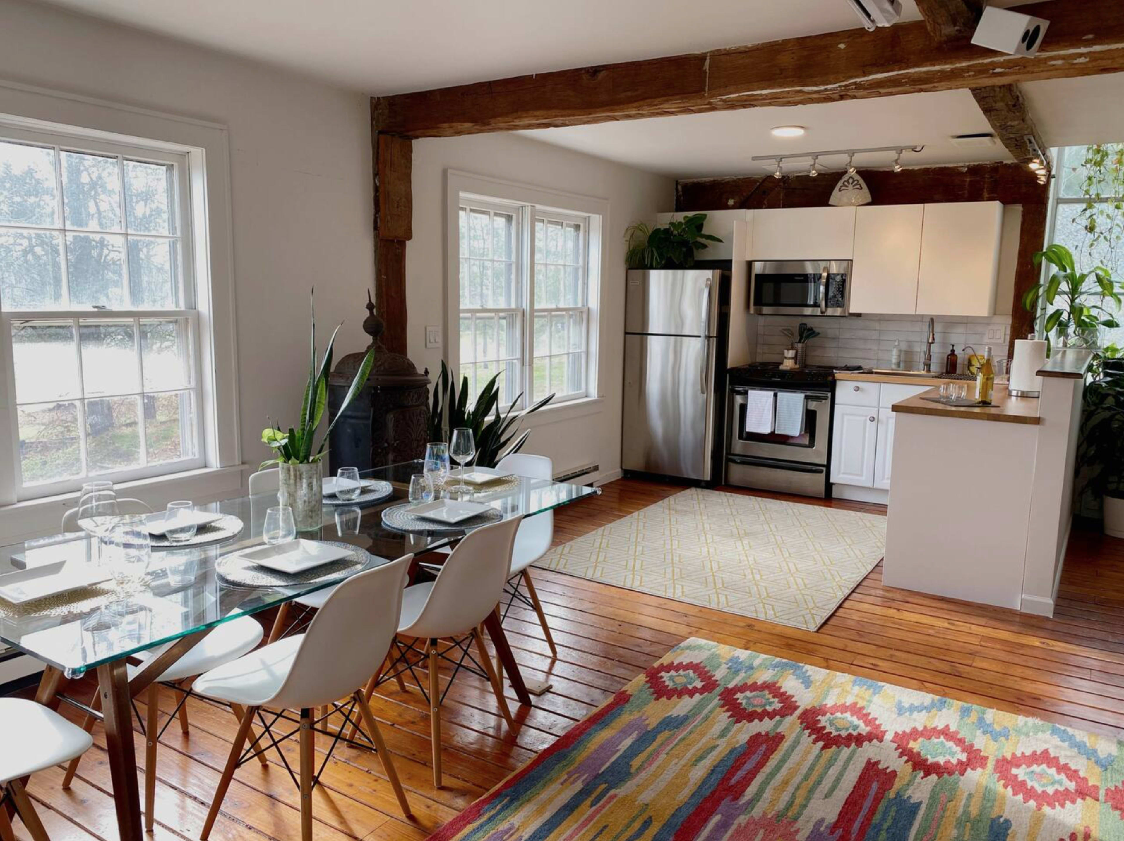 A modern kitchen and dining area with a glass dining table, white cabinets, stainless steel appliances, and wooden flooring.