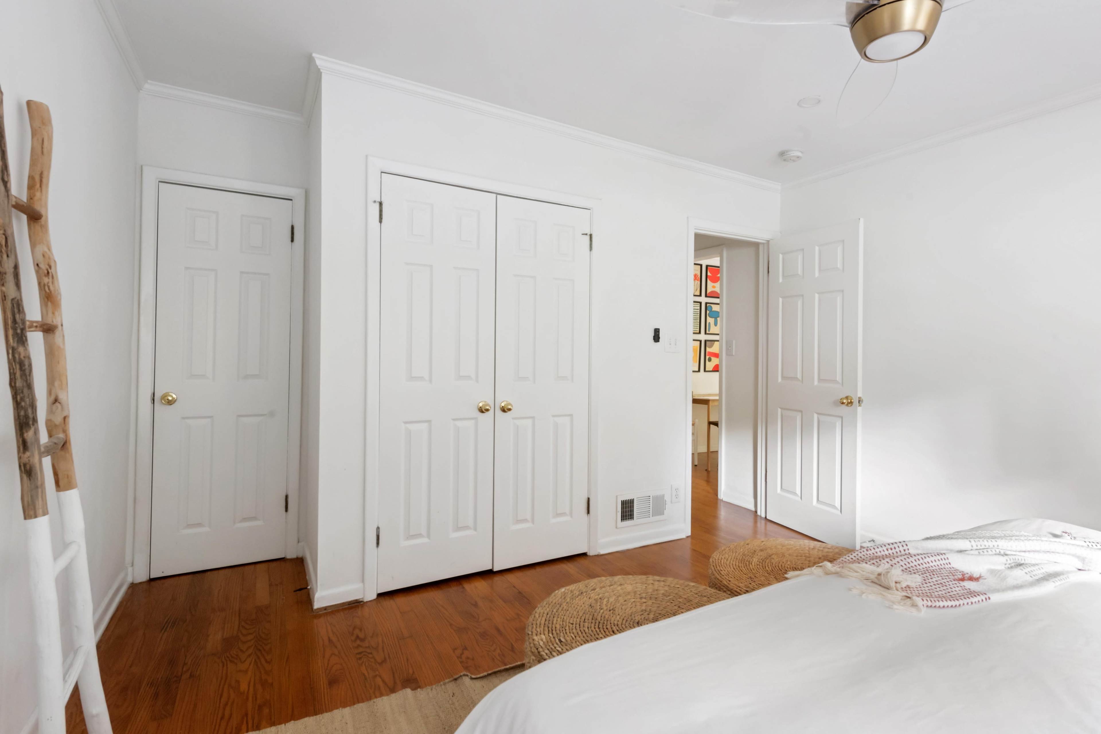 The image shows a minimalistic bedroom with white walls, two closed doors leading to closets, and a bed with a light-colored blanket.