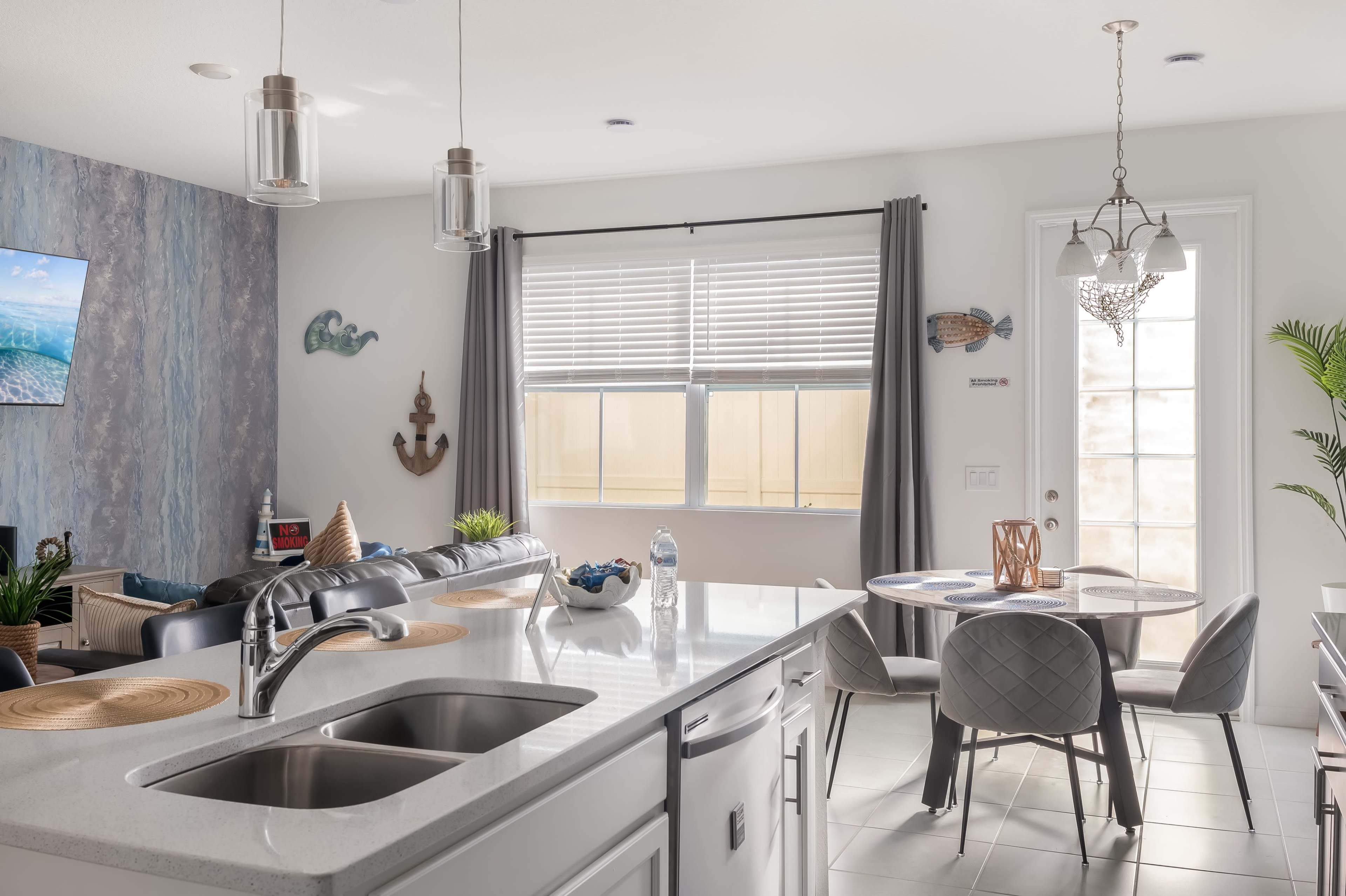 A modern kitchen features a central island with a sink, a dining area with a round table, and large windows providing natural light.