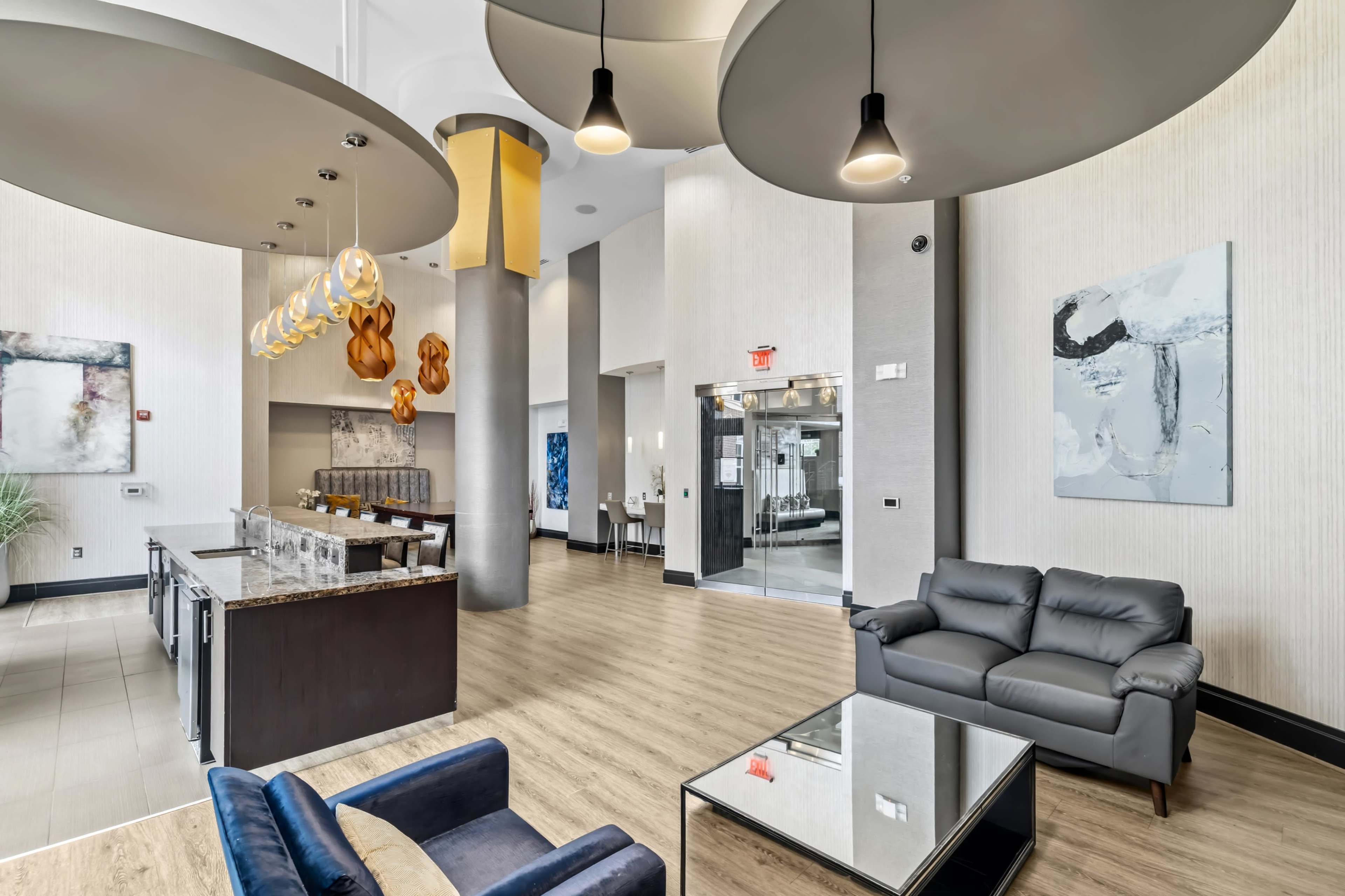 The image depicts a modern lobby with a reception area, featuring stylish furniture, pendant lighting, and a large glass elevator.