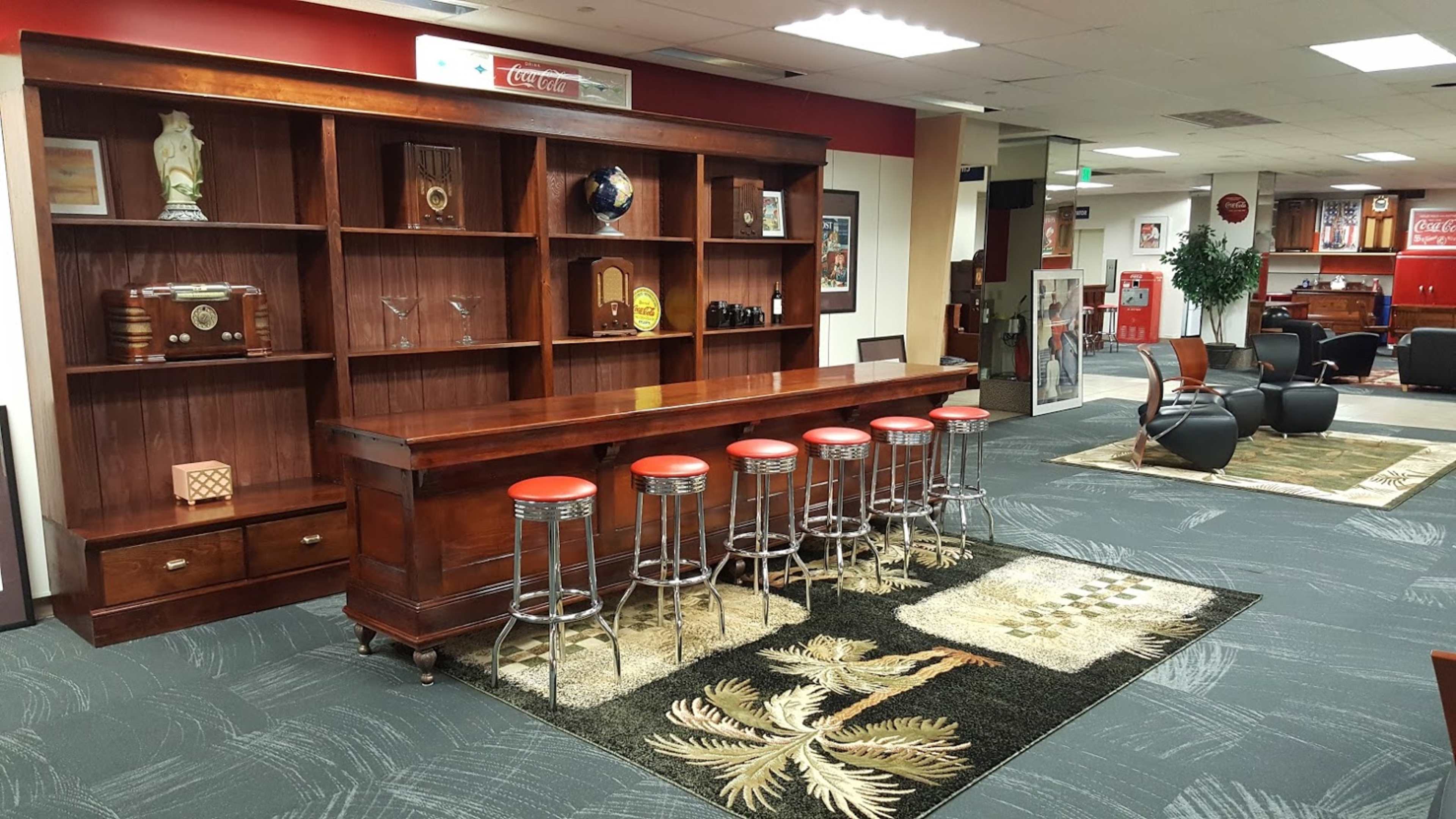 A wooden bar with red stools in front of a shelf filled with decorative items and a carpet featuring a leaf design.