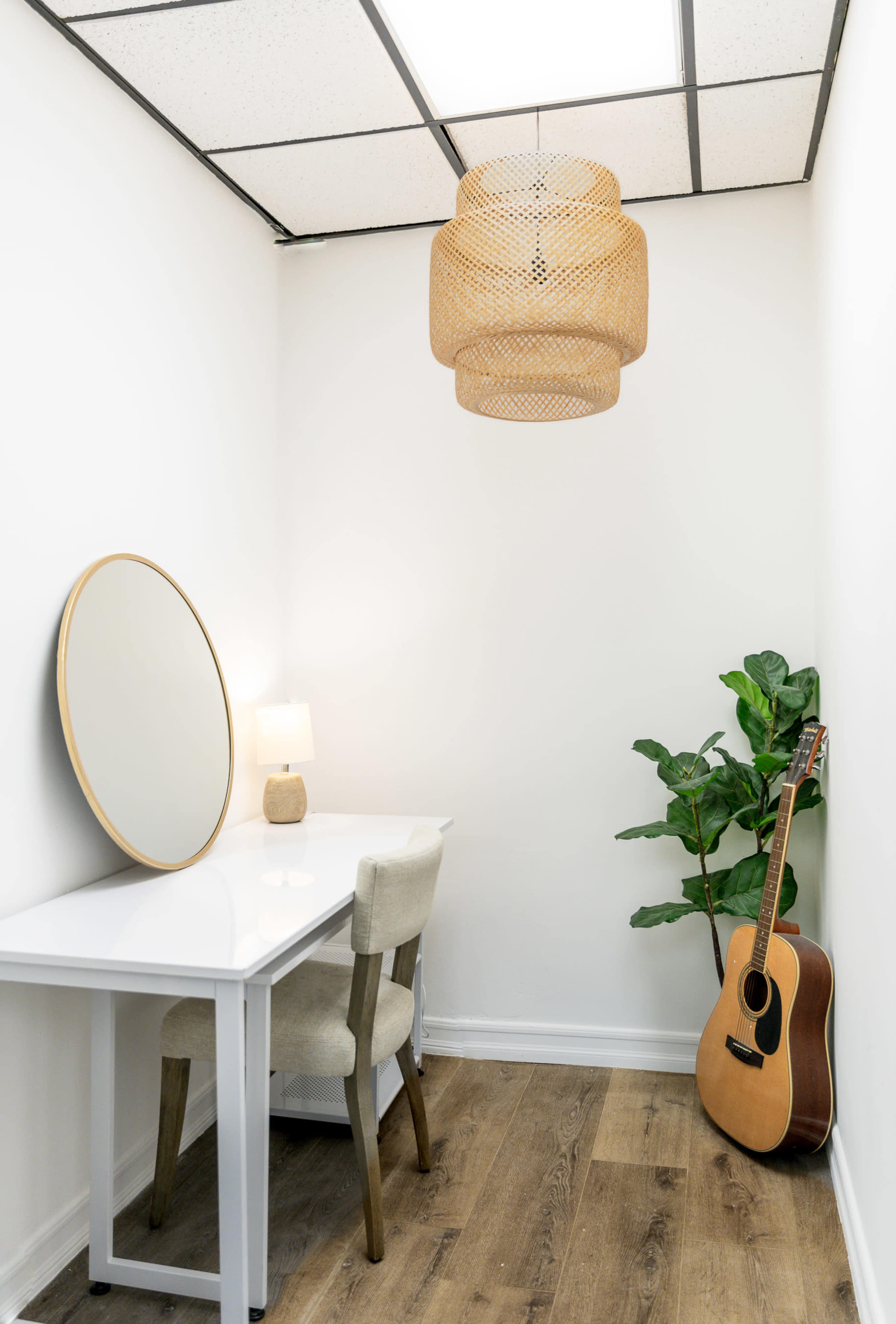 A small workspace features a white desk and chair, a round mirror on the wall, a lamp, a potted plant, and an acoustic guitar leaning against the wall.
