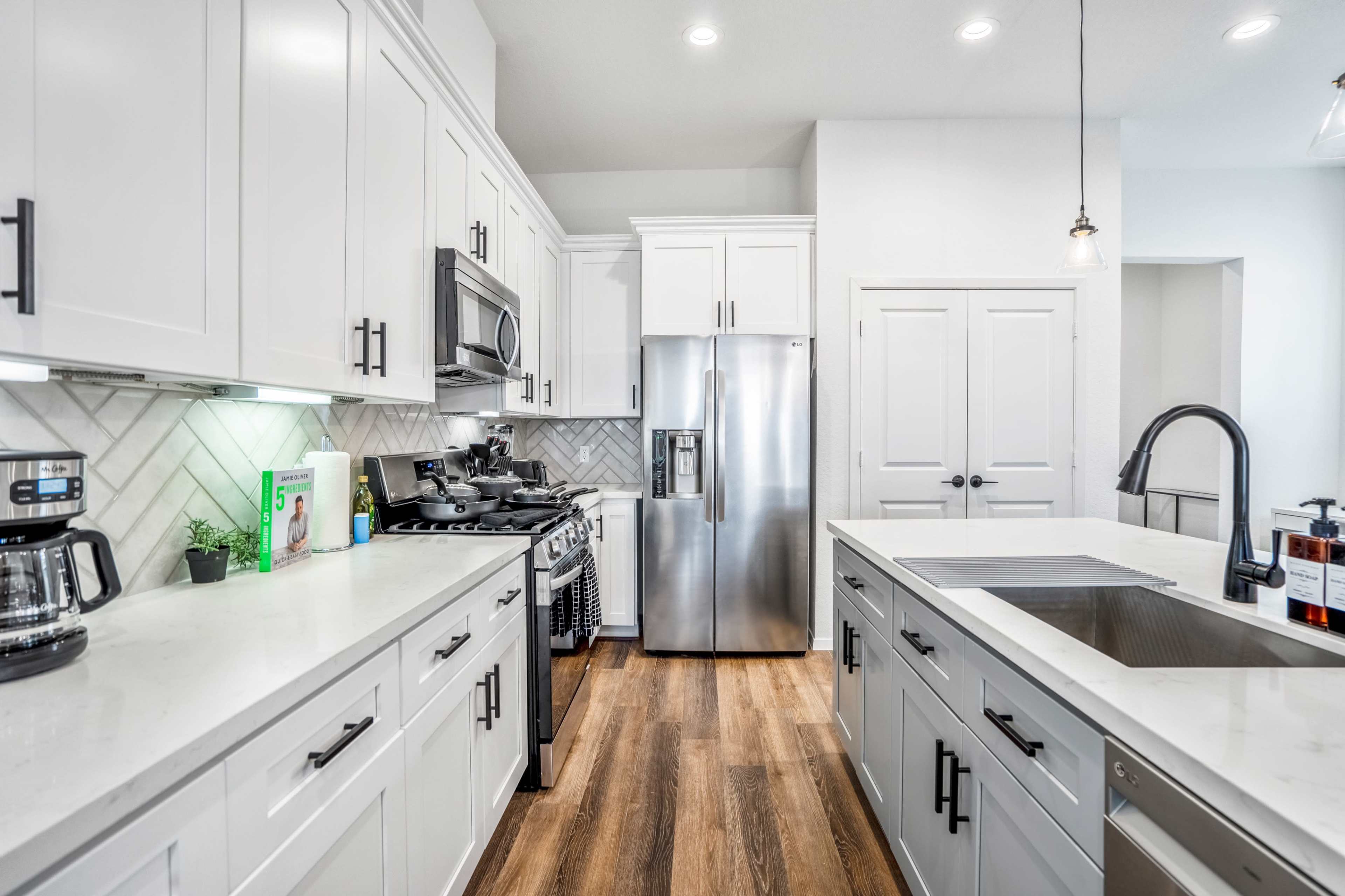 A modern kitchen features white cabinetry, stainless steel appliances, and a large island with a sink, complemented by wood flooring.