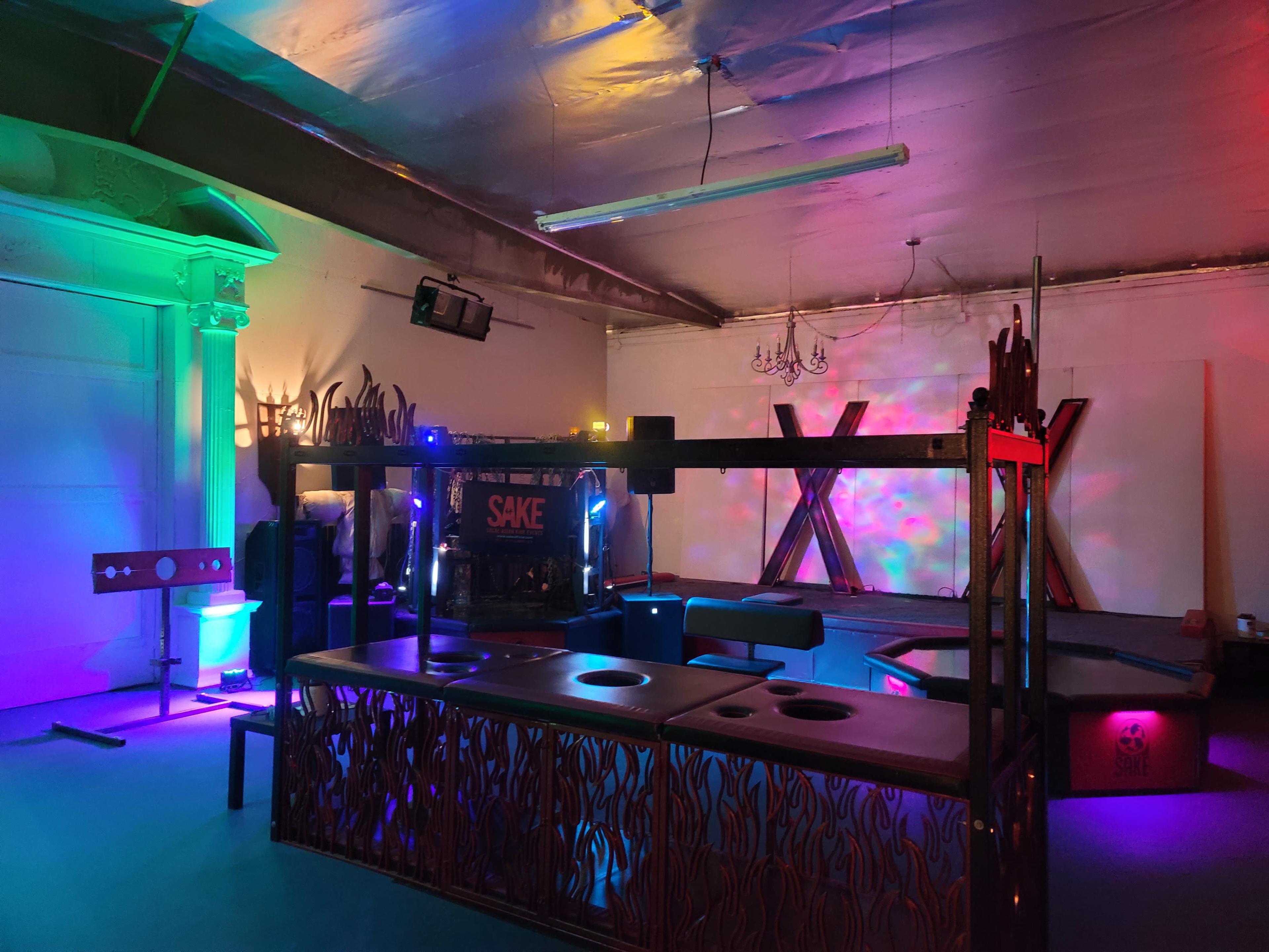 A dimly lit room with colorful lighting, featuring a bar area and decorative elements against the walls.