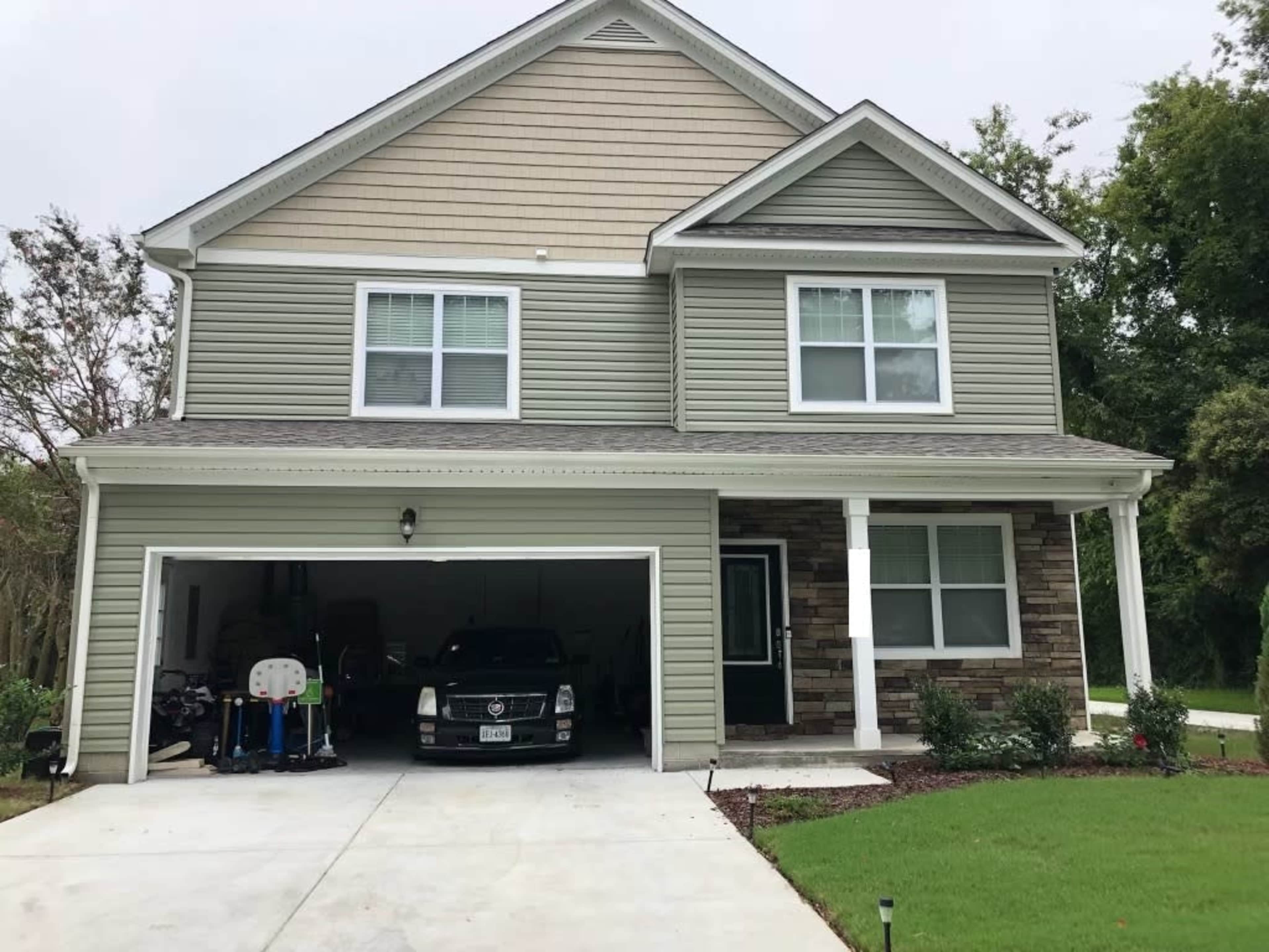 A two-story house with green siding and a stone facade, featuring a garage with a car parked inside.