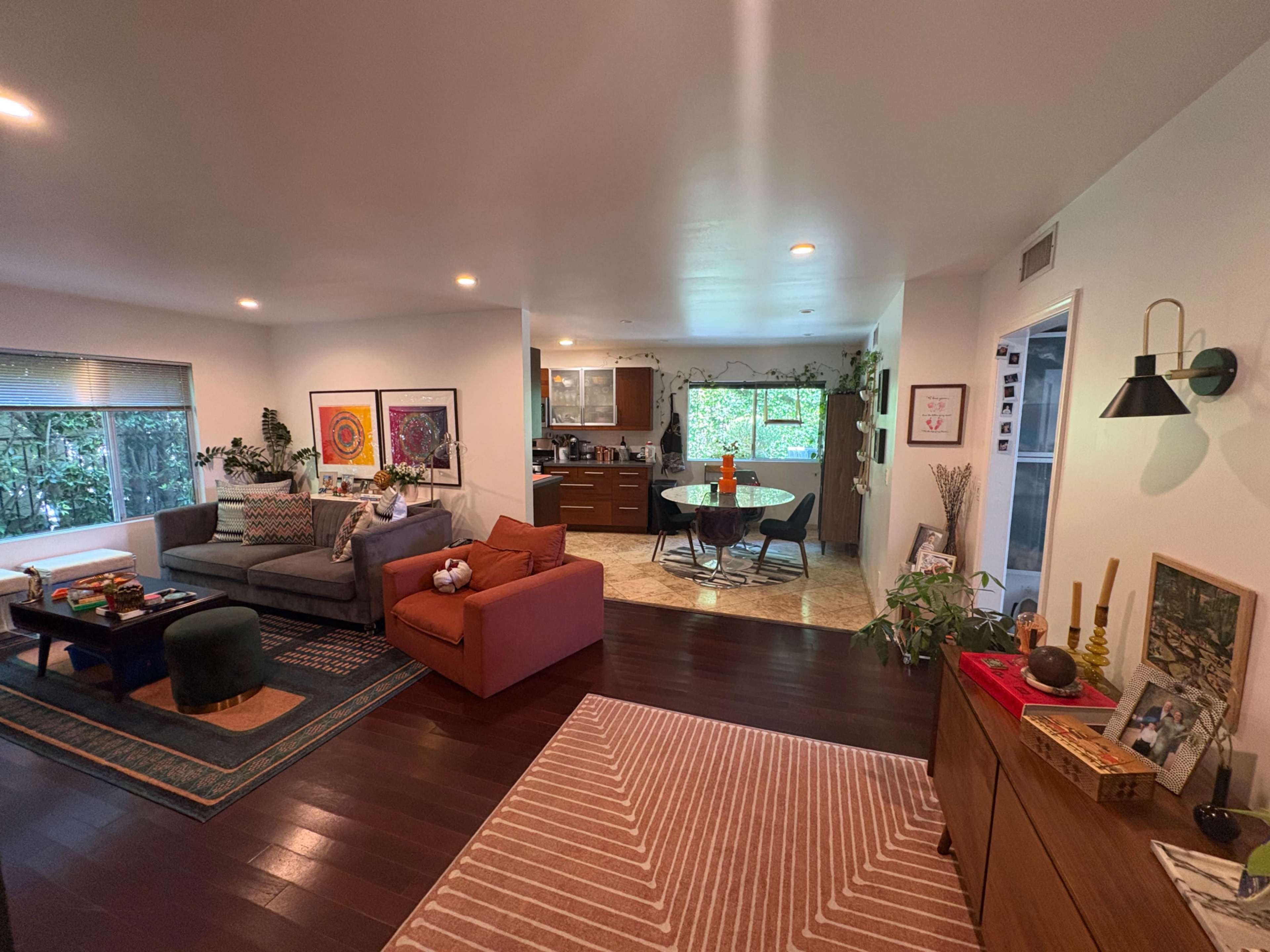 The image shows a modern living room and kitchen area featuring a sofa, a dining table, and various decorative elements.