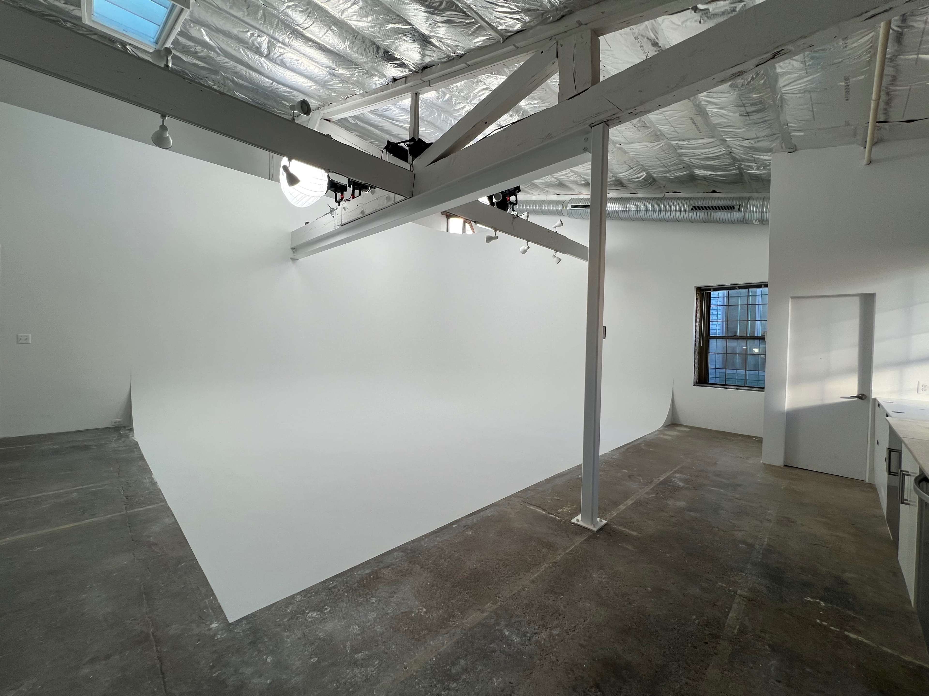 A spacious, empty studio with a curved white backdrop and large windows.