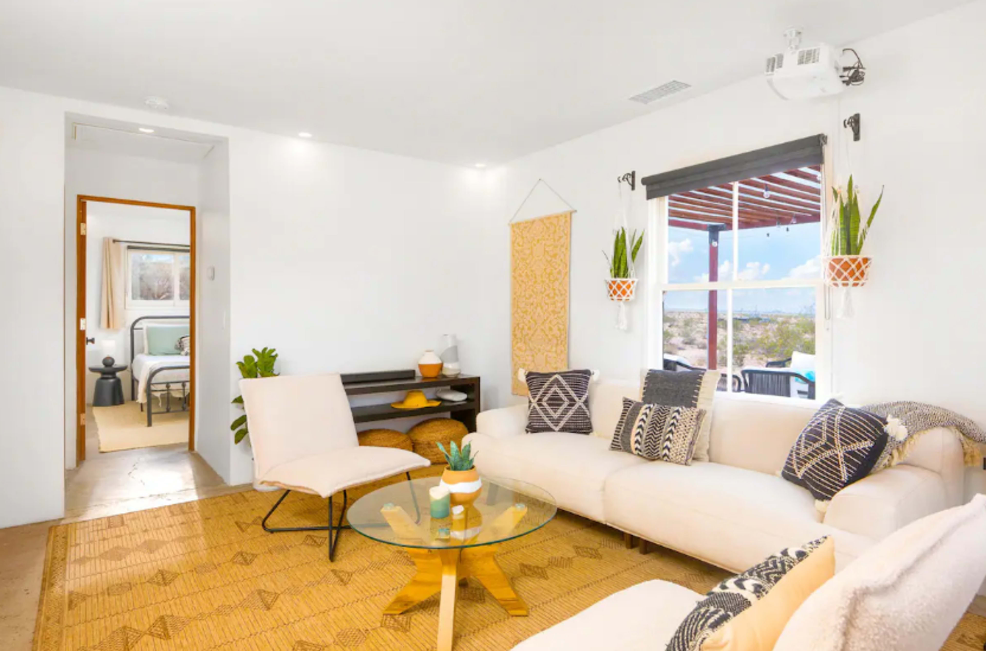 The image shows a modern living room with a white sofa, a glass coffee table, and a view of a patio through a sliding door.