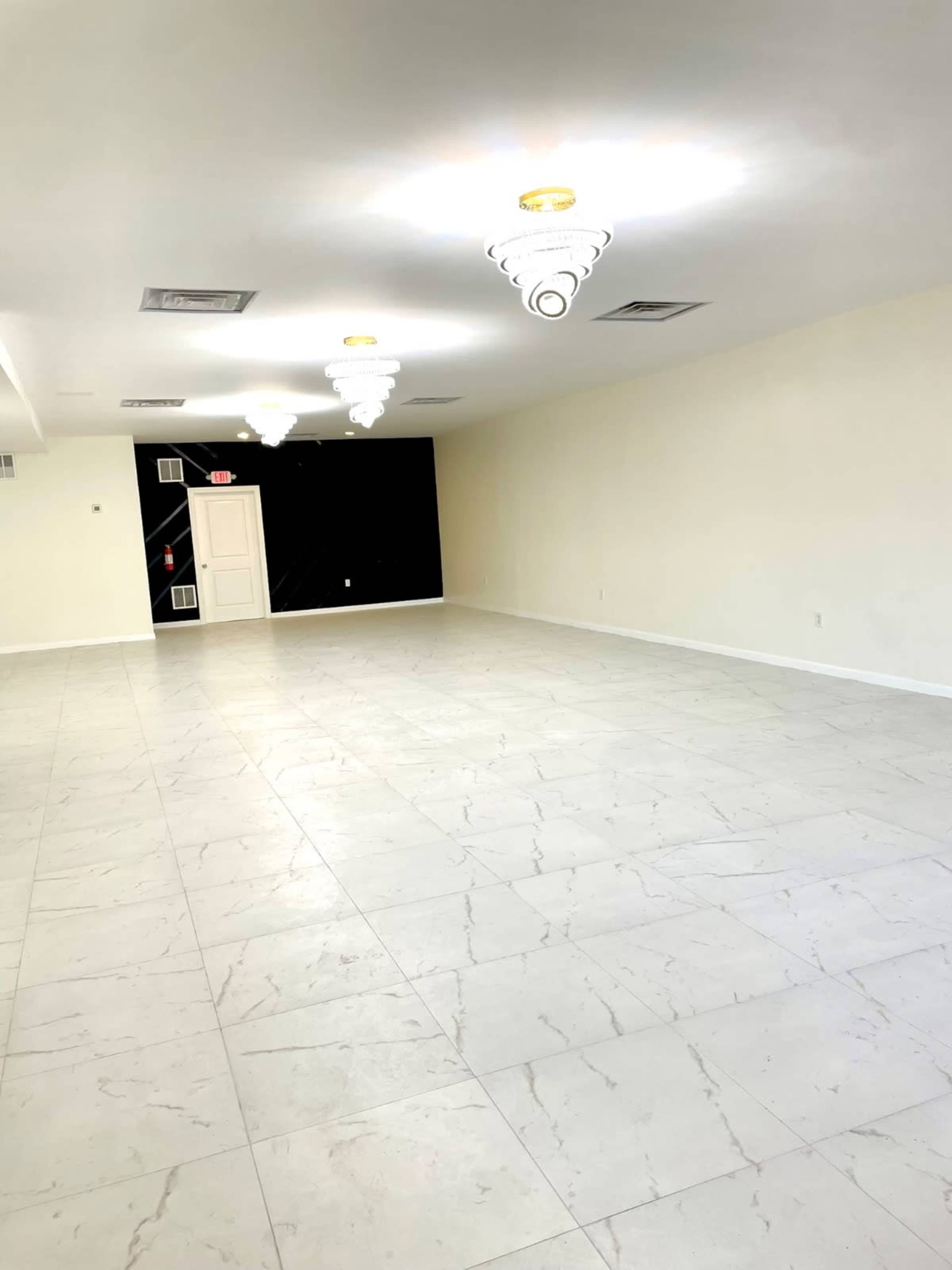 A spacious, empty room with white tiled flooring and decorative ceiling lights.