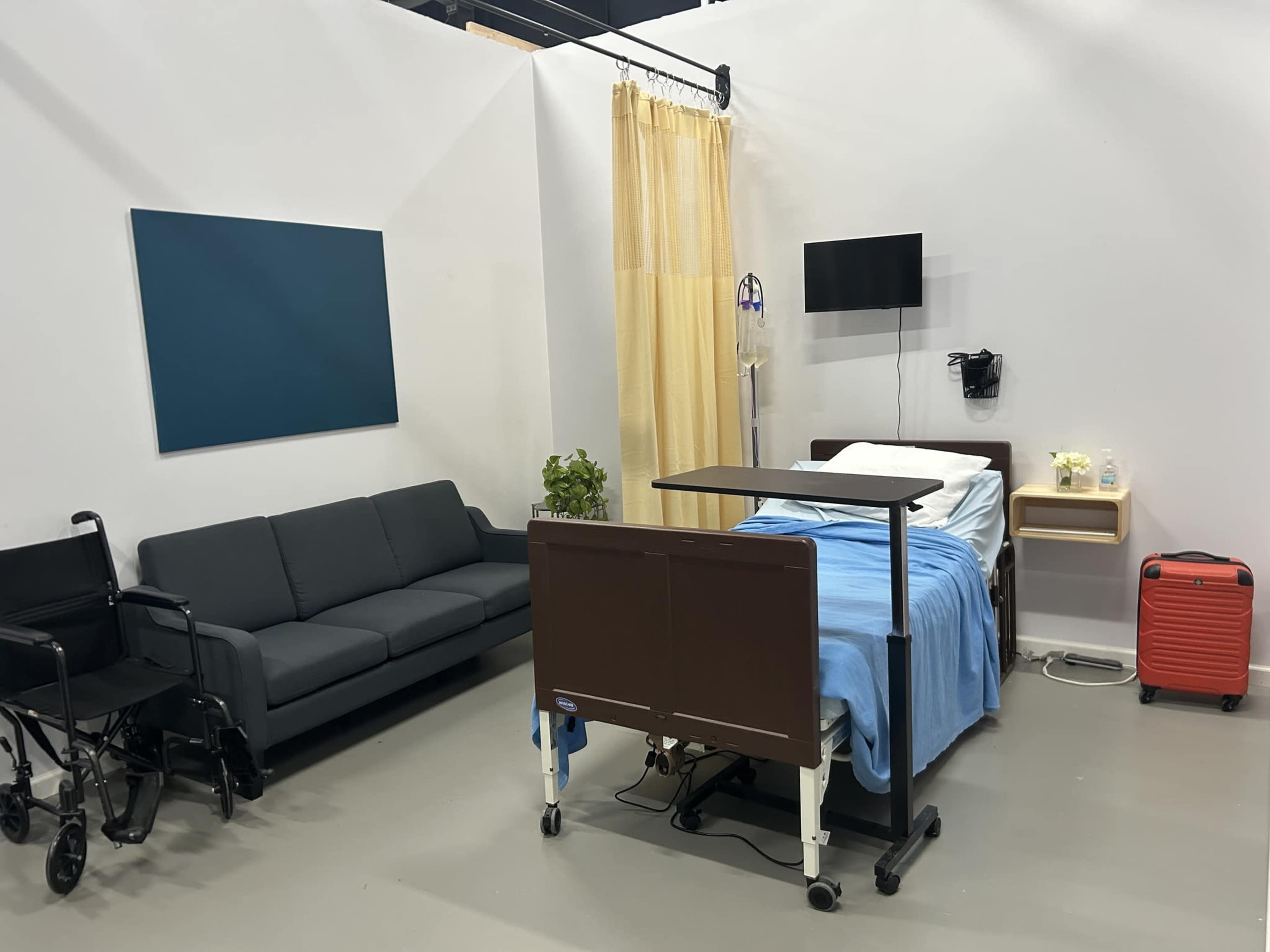 The image shows a hospital room equipped with a bed, a couch, a privacy curtain, a television, and medical equipment.