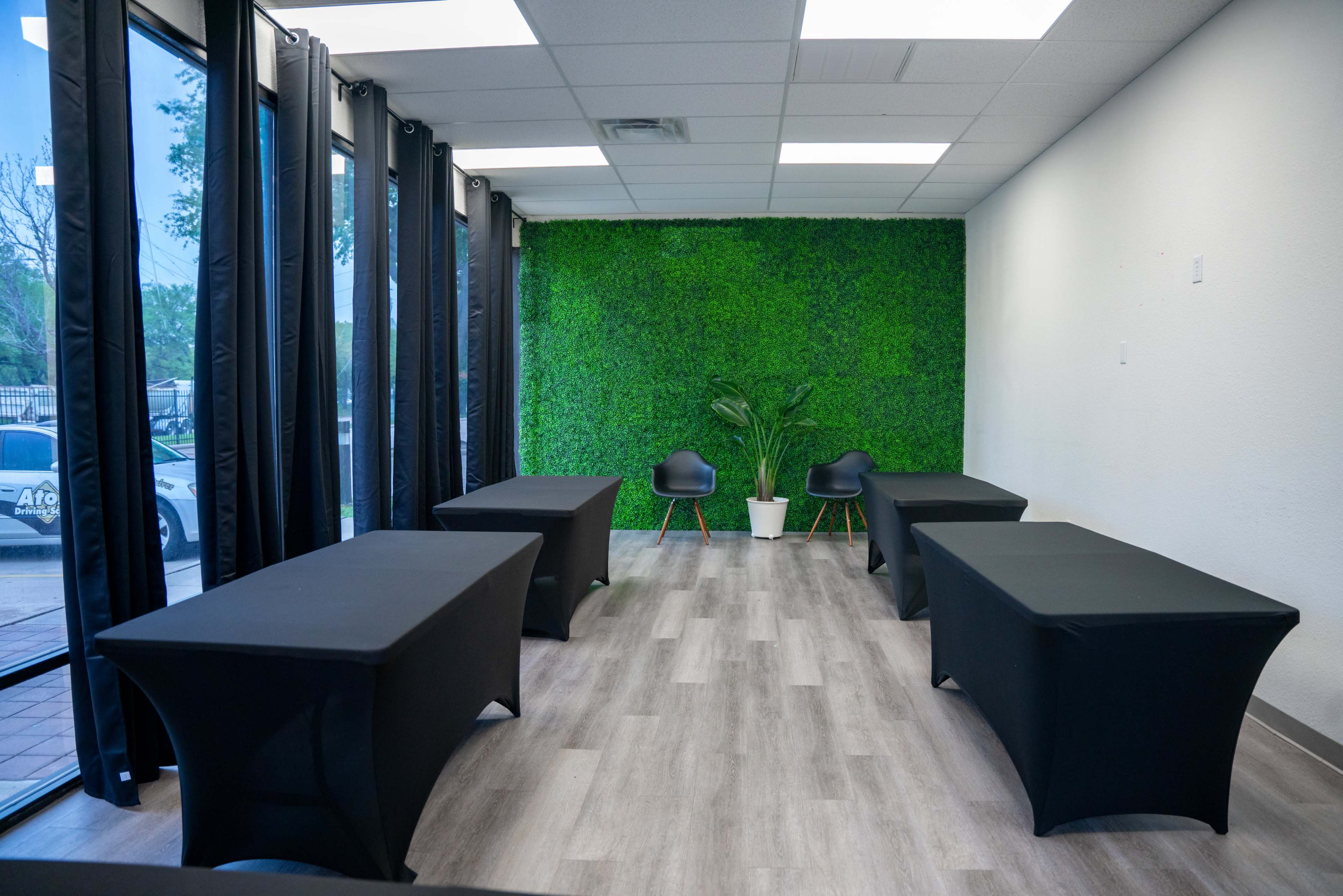 A well-lit room with black tables, two chairs, and a green wall made of artificial foliage.