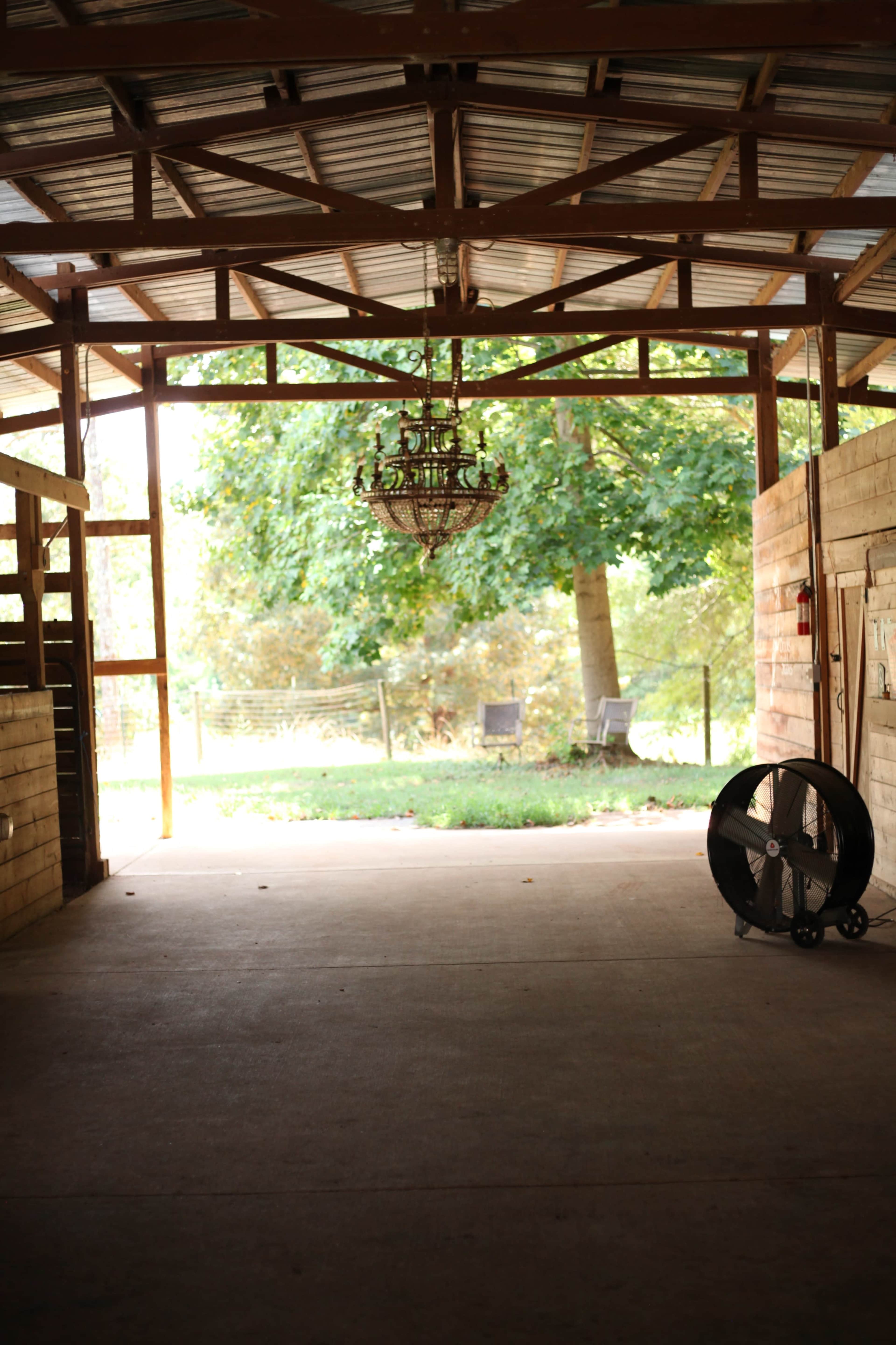 The image shows the interior of a barn with a chandelier hanging from the ceiling, illuminated by natural light coming from an opening at the far end.