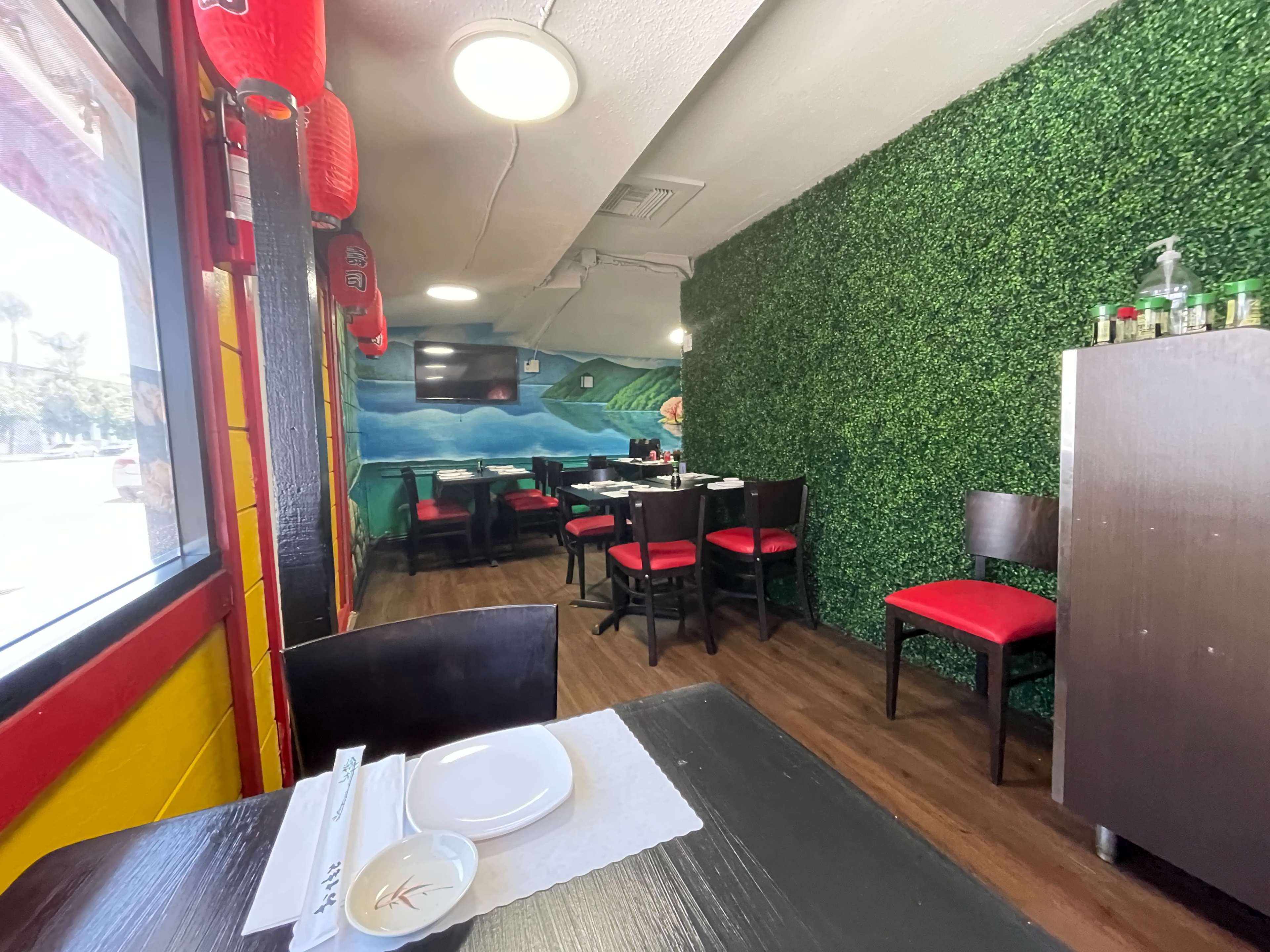 The image shows the interior of a restaurant with green wall decor, tables set for dining, and a television mounted on the wall.