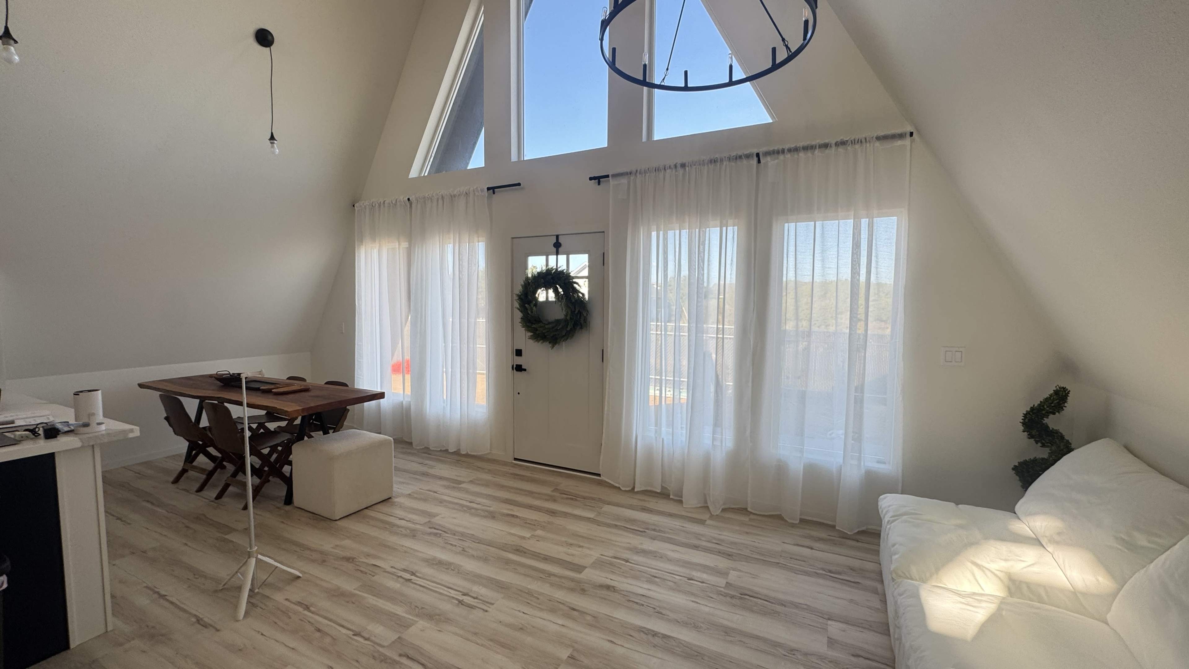 The image shows a spacious, well-lit room with high ceilings, large windows, a dining table, and a white couch.
