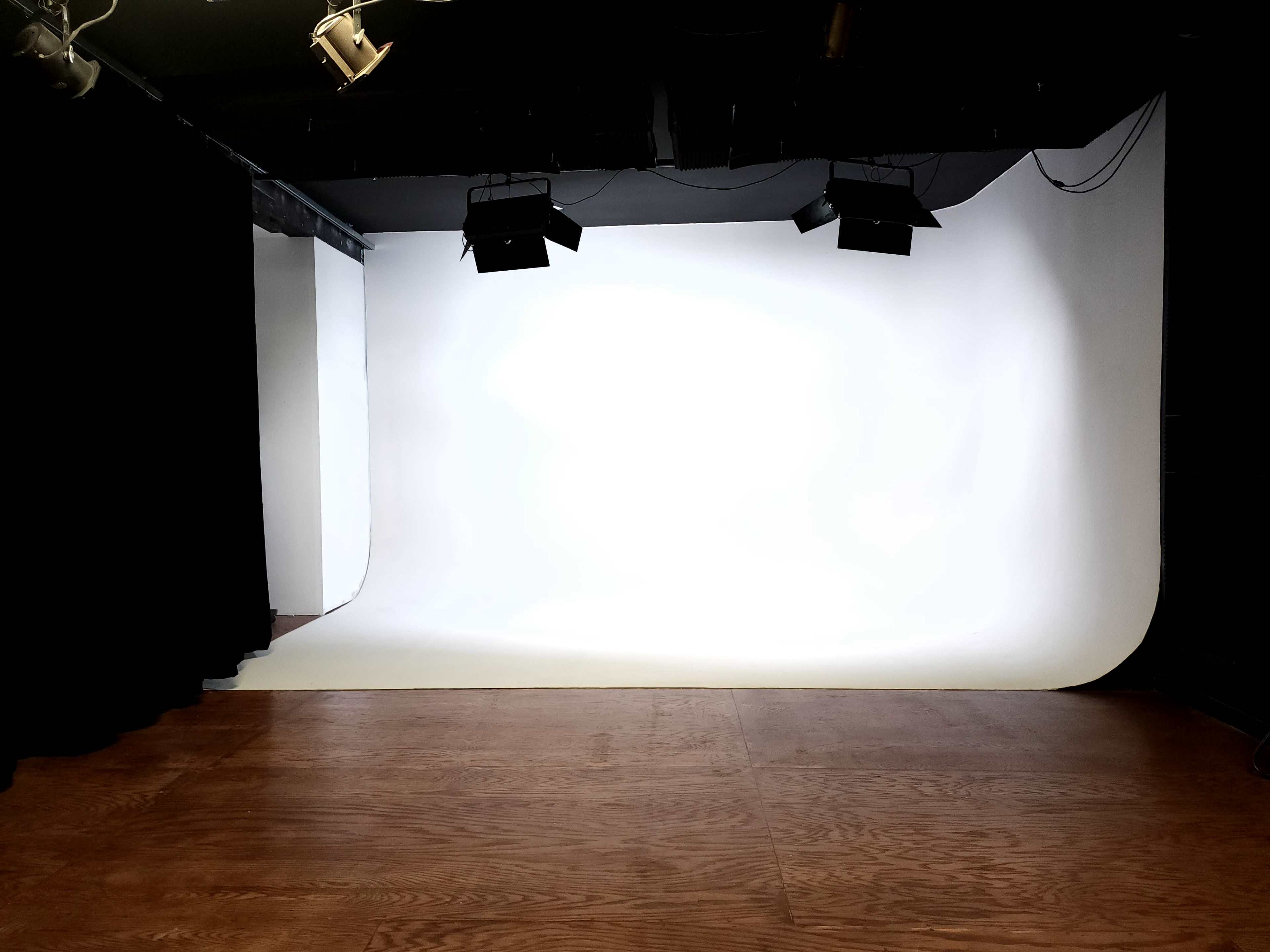 A photography studio features a seamless white backdrop with wooden flooring and black curtains.
