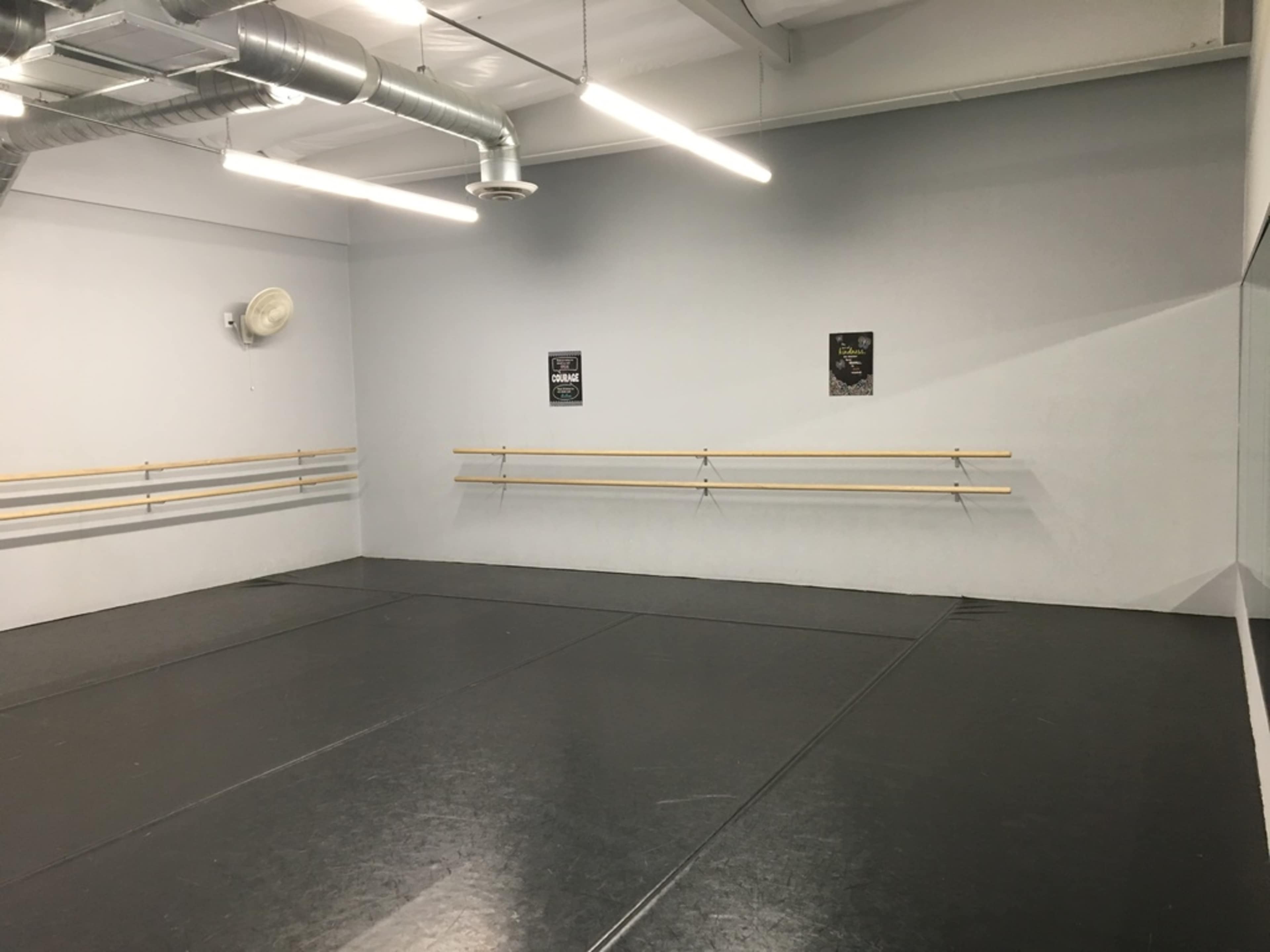 A dance studio with a black floor, mirrored wall, and two posters on the gray wall.