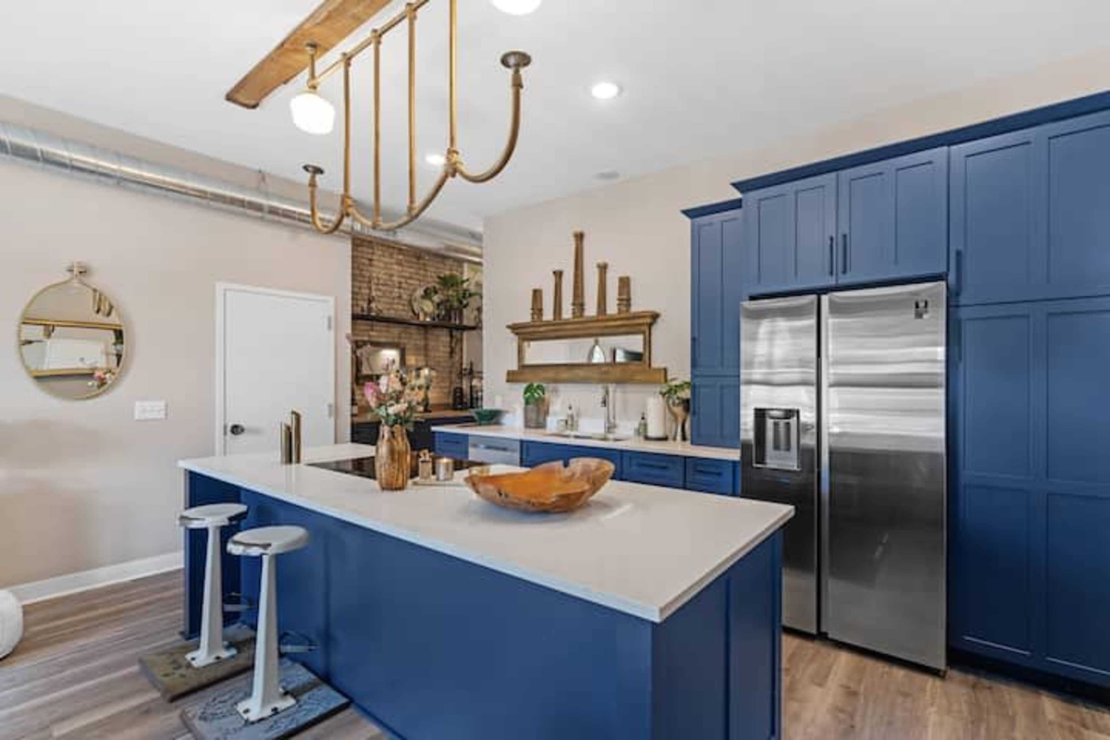 A modern kitchen features navy blue cabinetry, a large island with a wood bowl centerpiece, and stainless steel appliances.