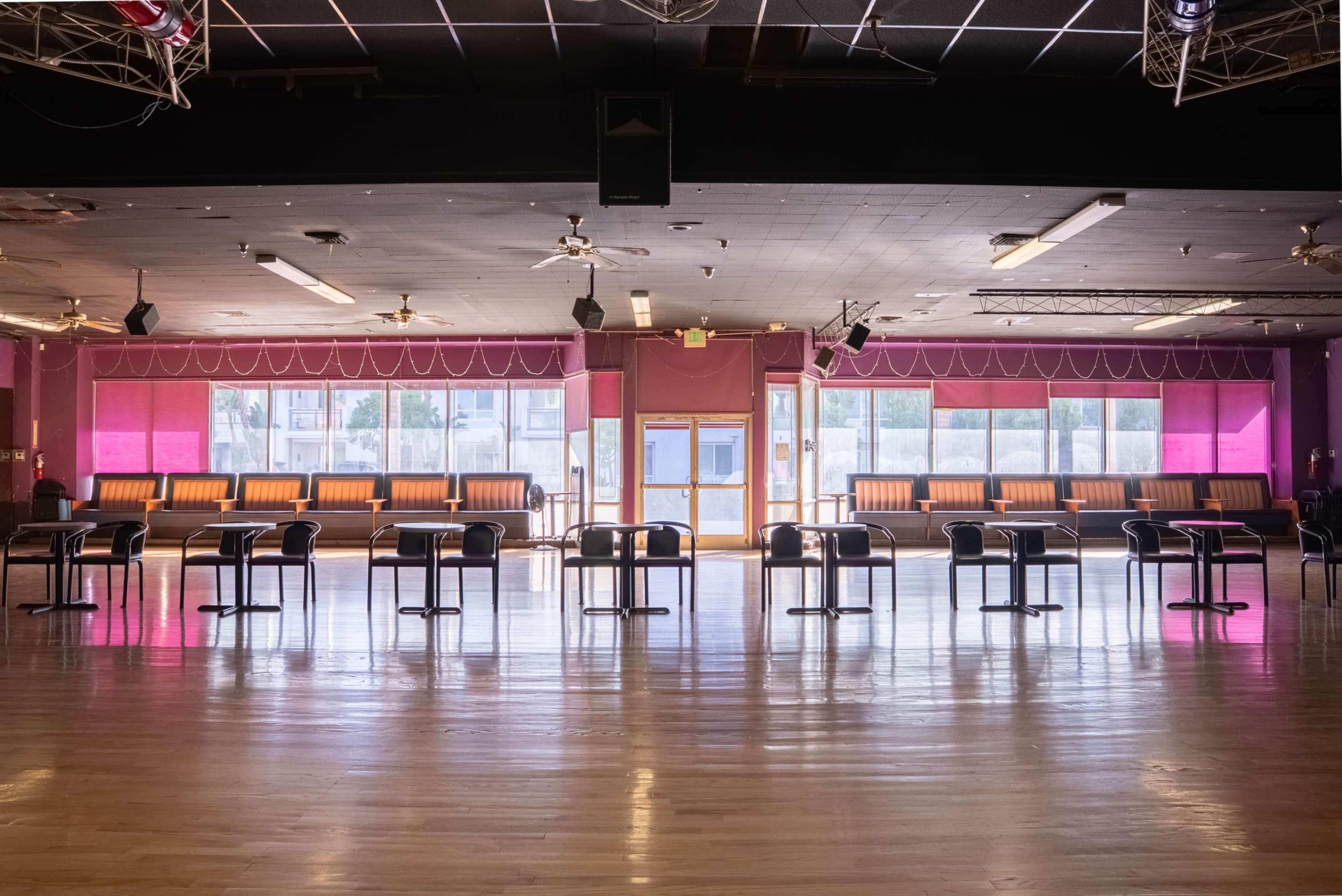 The image shows an empty dance studio with rows of chairs facing a large window, illuminated by natural light.