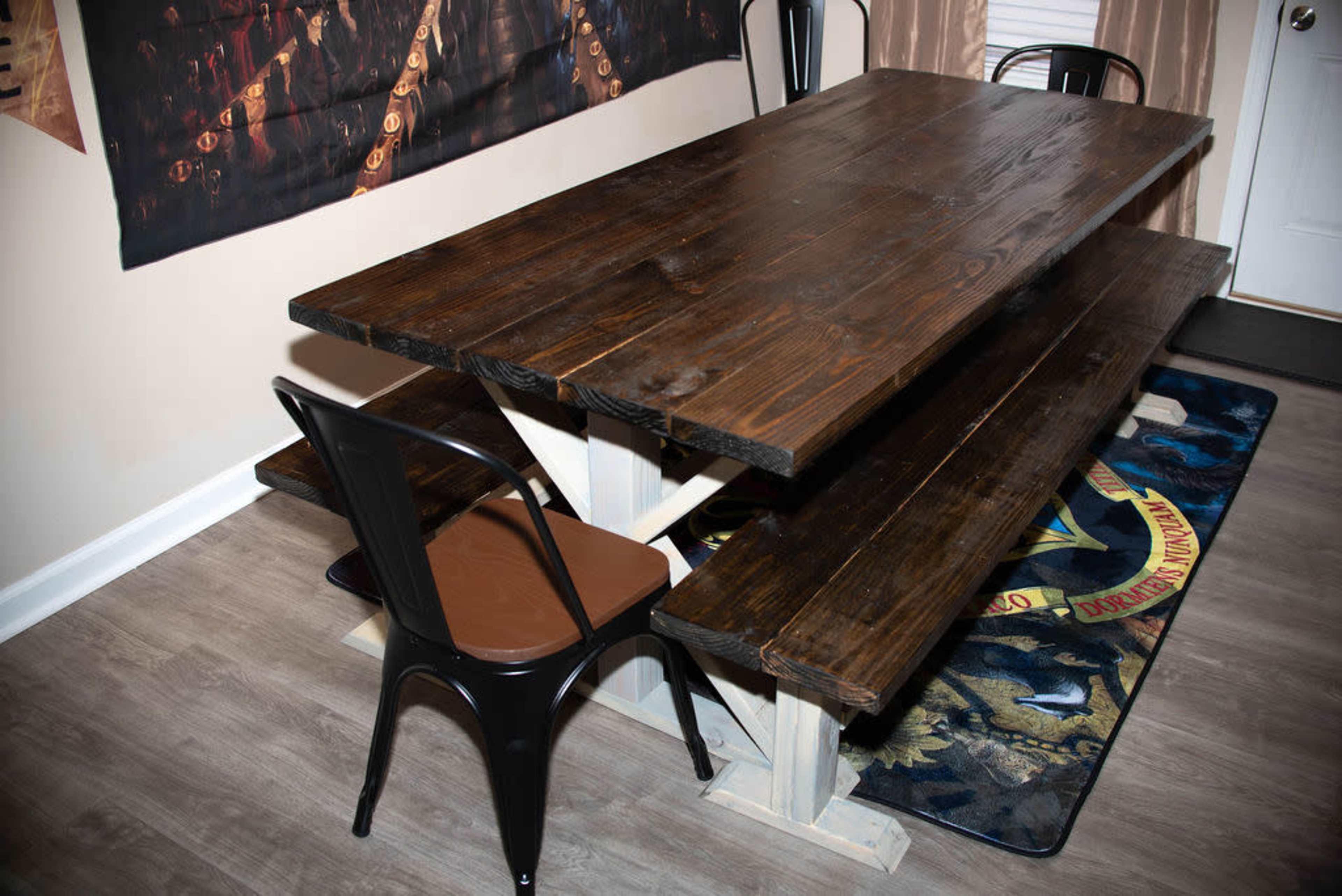 A wooden dining table with two matching benches and a single chair positioned nearby, set against a wall adorned with a decorative poster.