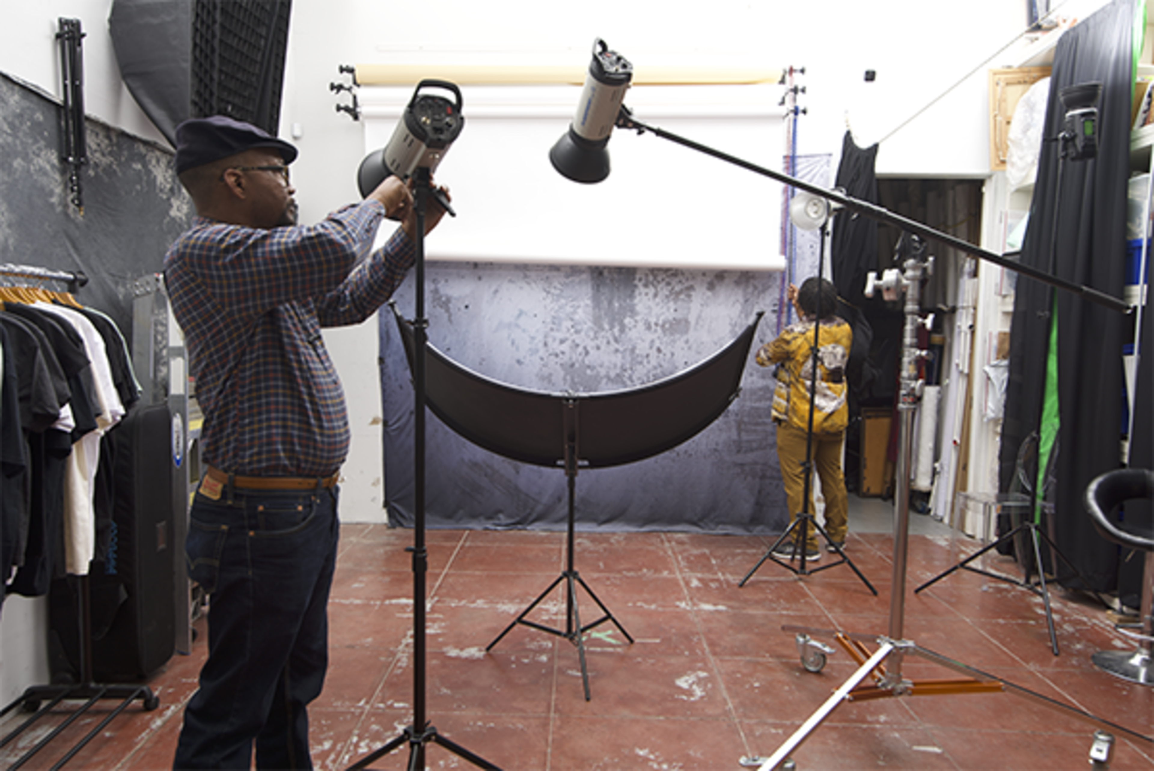 A photographer is adjusting a lighting setup in a studio while another person prepares a backdrop.