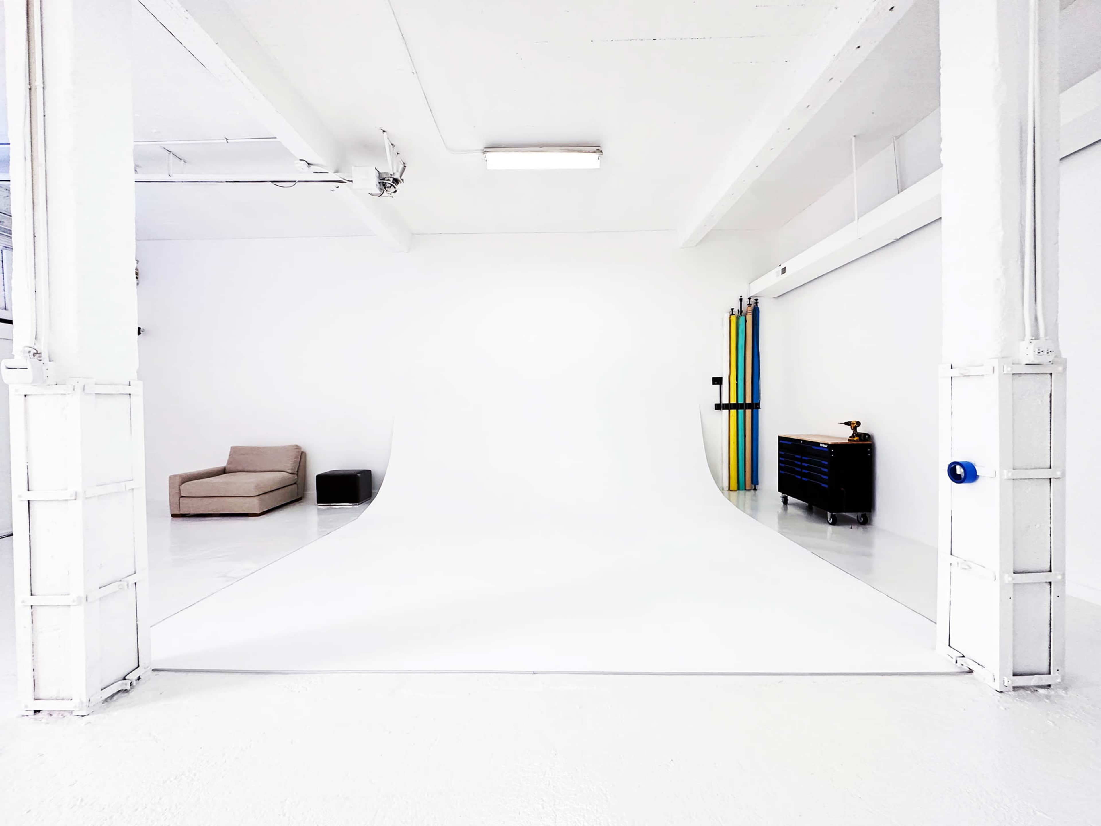 A spacious, minimalist studio with a white backdrop, a couch, a black storage box, and a tool chest against the wall.