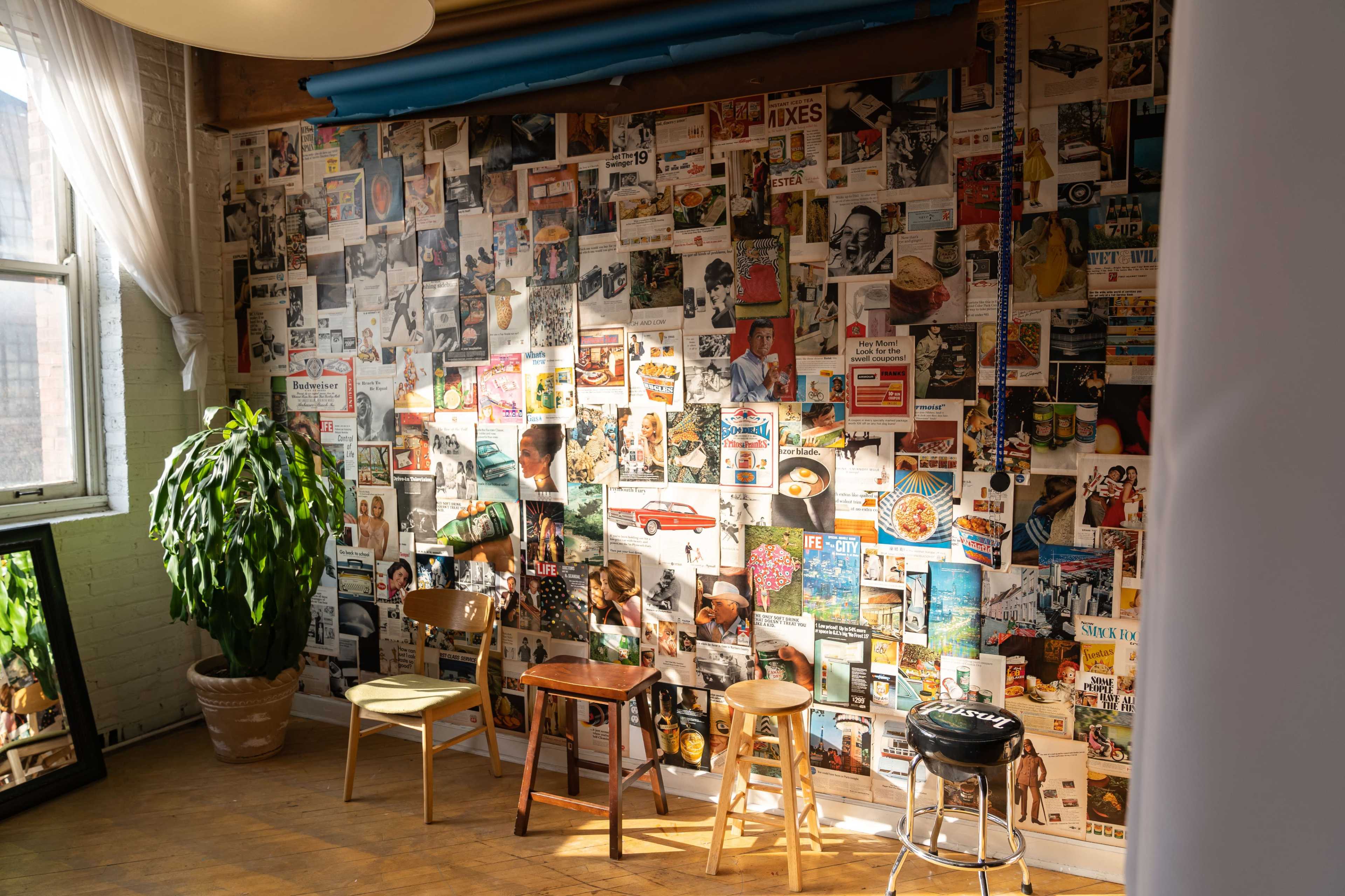 A cozy room with a wall covered in vintage magazine clippings and three wooden chairs positioned in front of it.