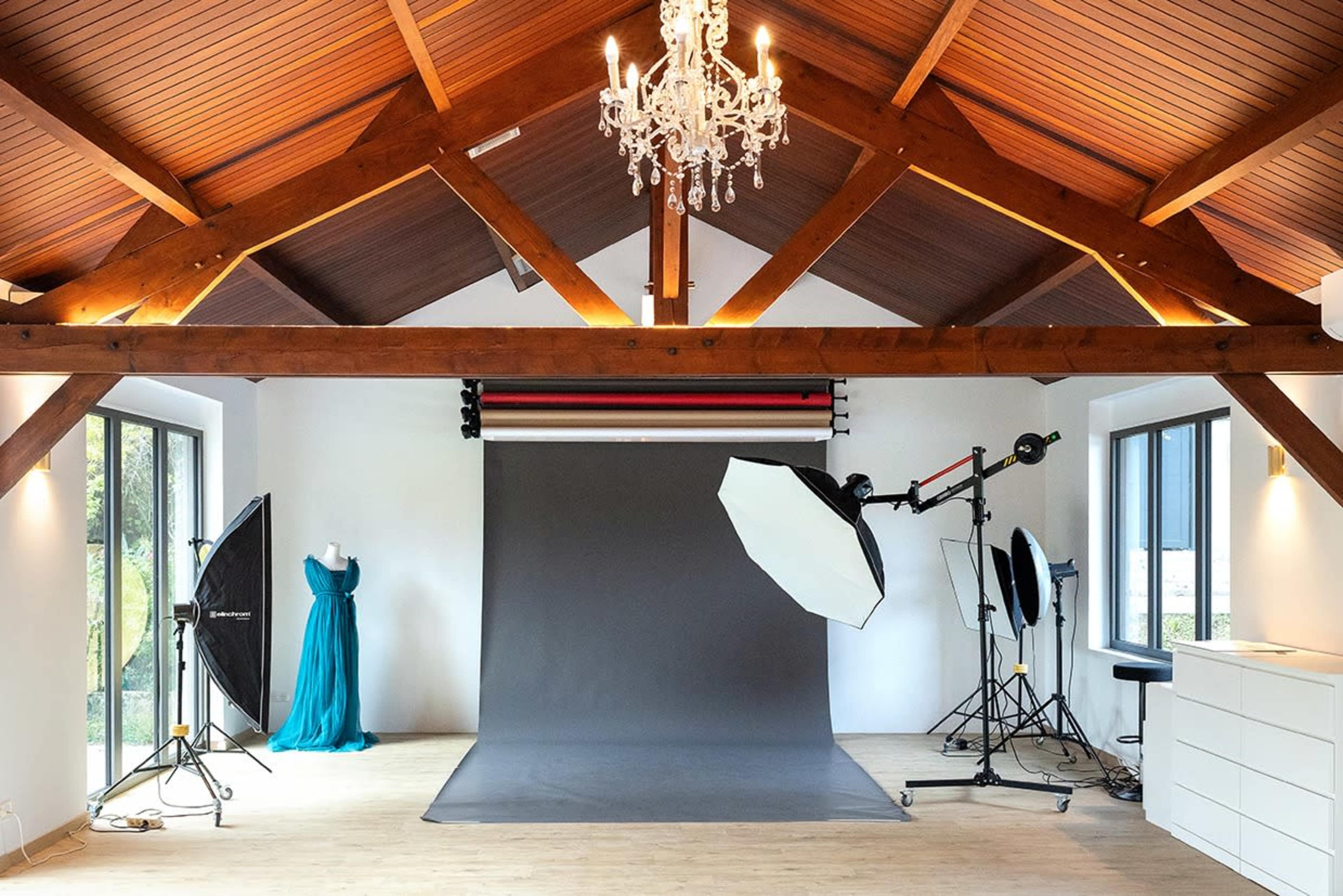 The image shows a photography studio with a gray backdrop, a mannequin draped in a blue dress, and various lighting equipment arranged around the space.