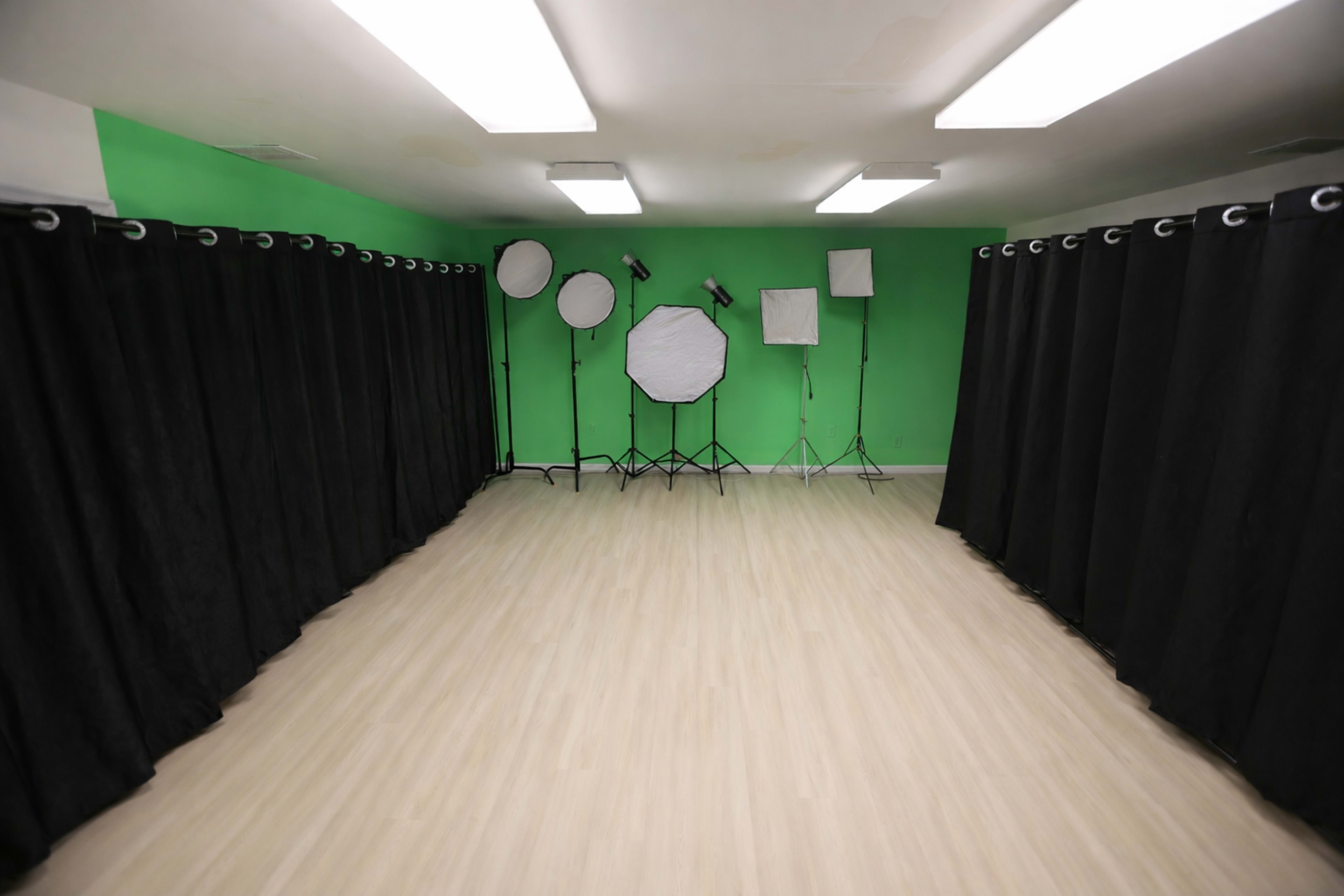 The image shows a photography studio with a green wall, black curtains, and various lighting setups.