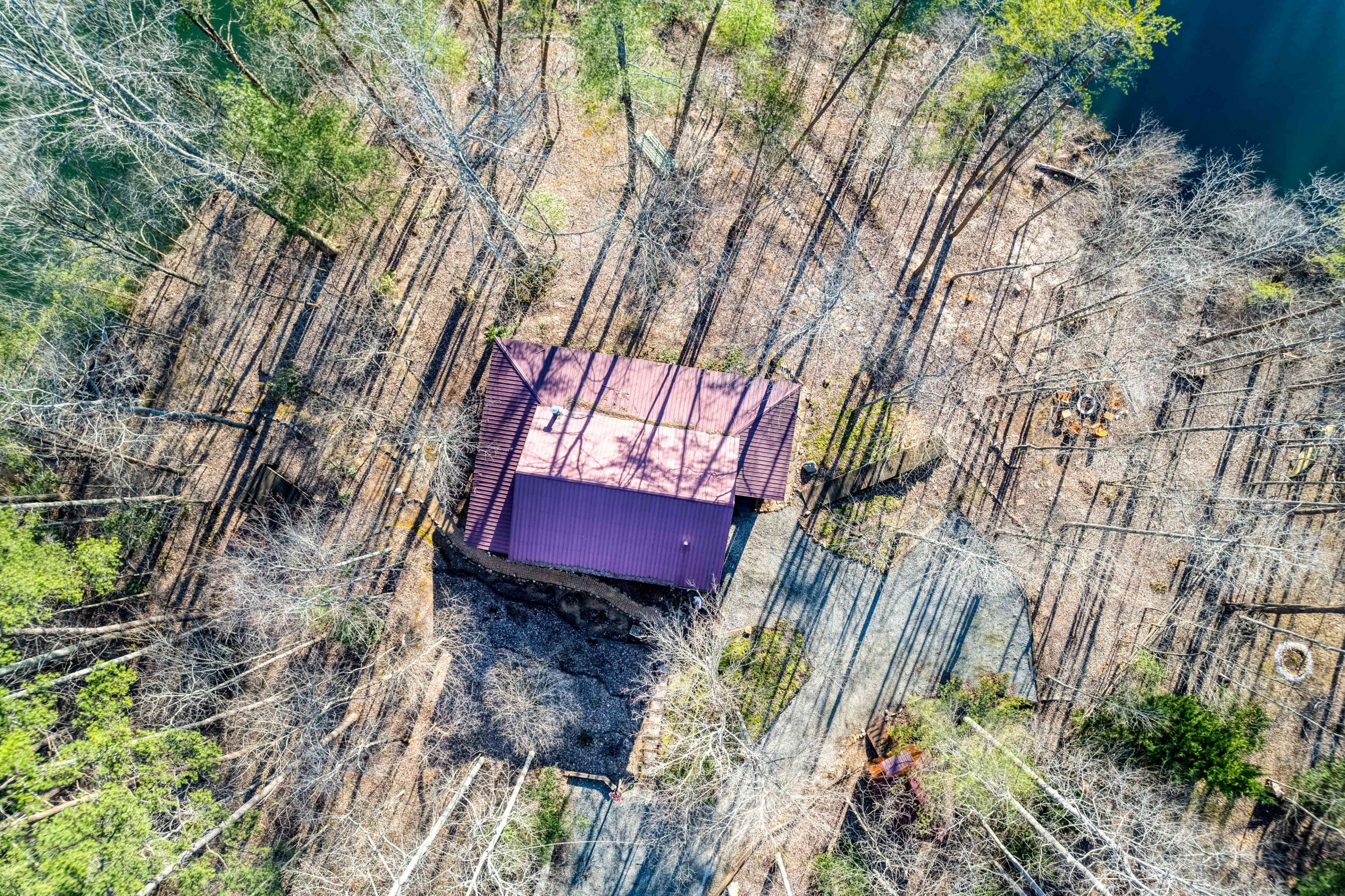 An aerial view shows a house with a red roof surrounded by bare trees and a pond nearby.
