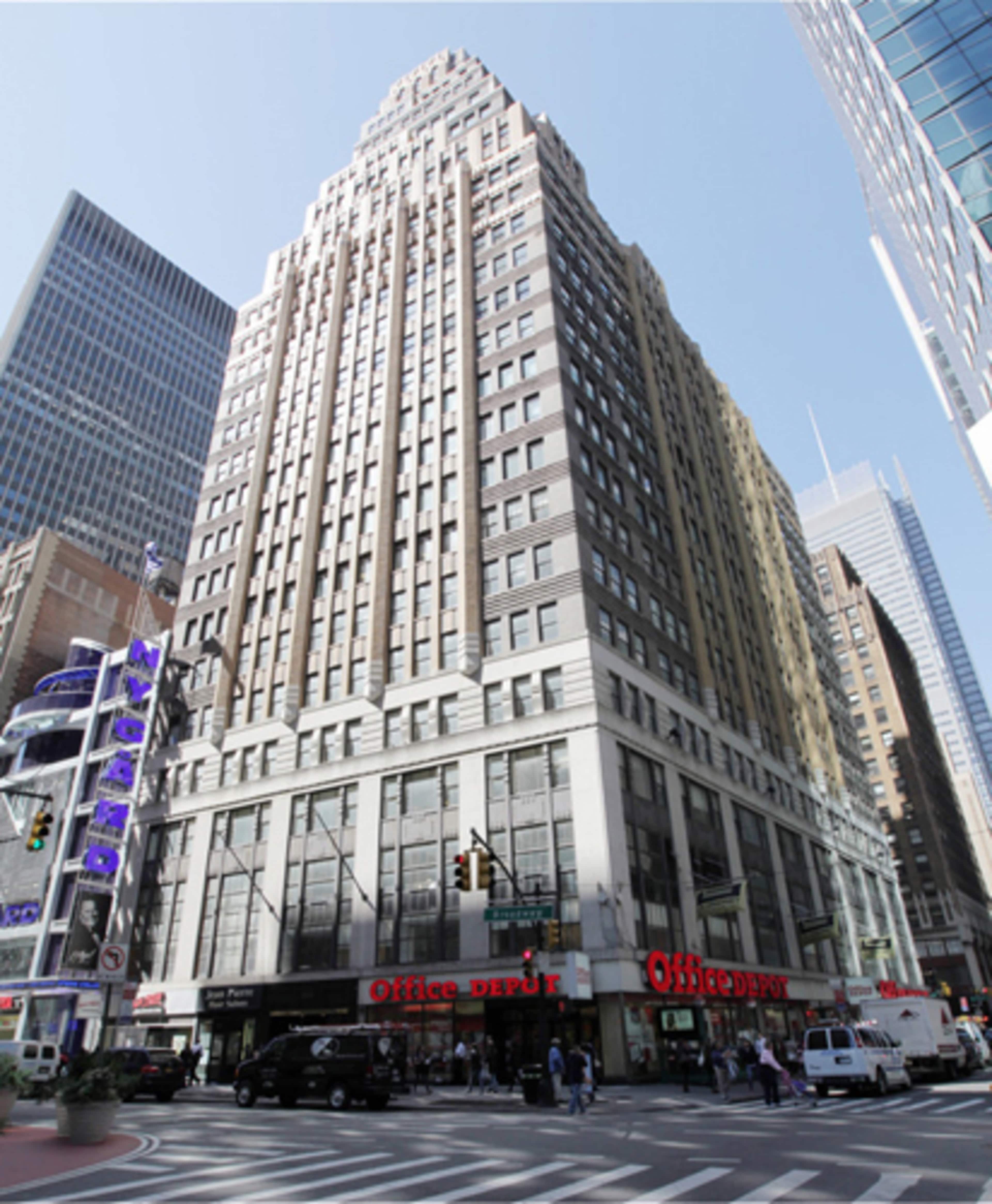 A tall Art Deco building with a triangular top stands on a busy corner, featuring an Office Depot store at its base.
