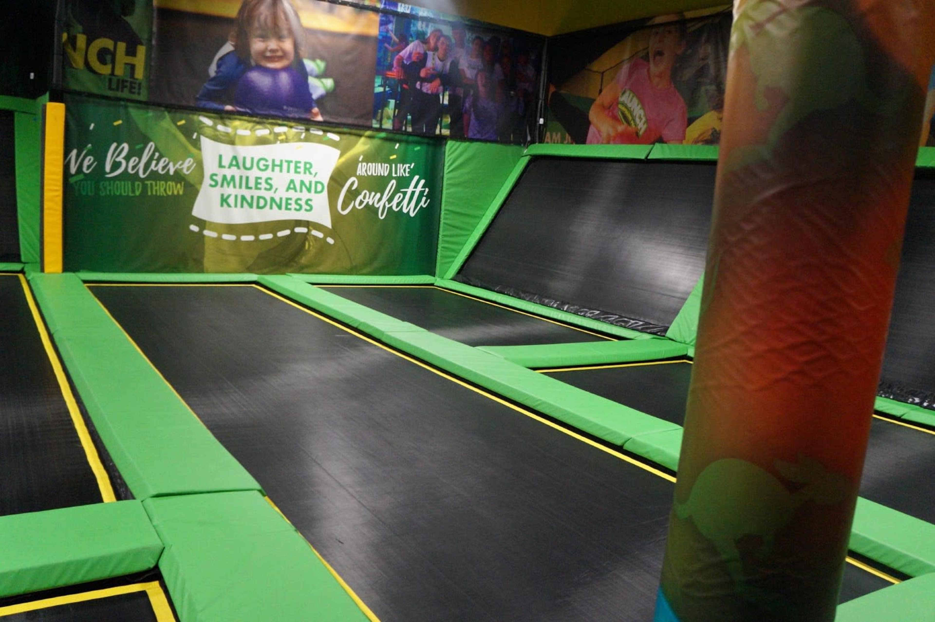 A brightly colored indoor trampoline park featuring multiple trampolines surrounded by vibrant wall banners.