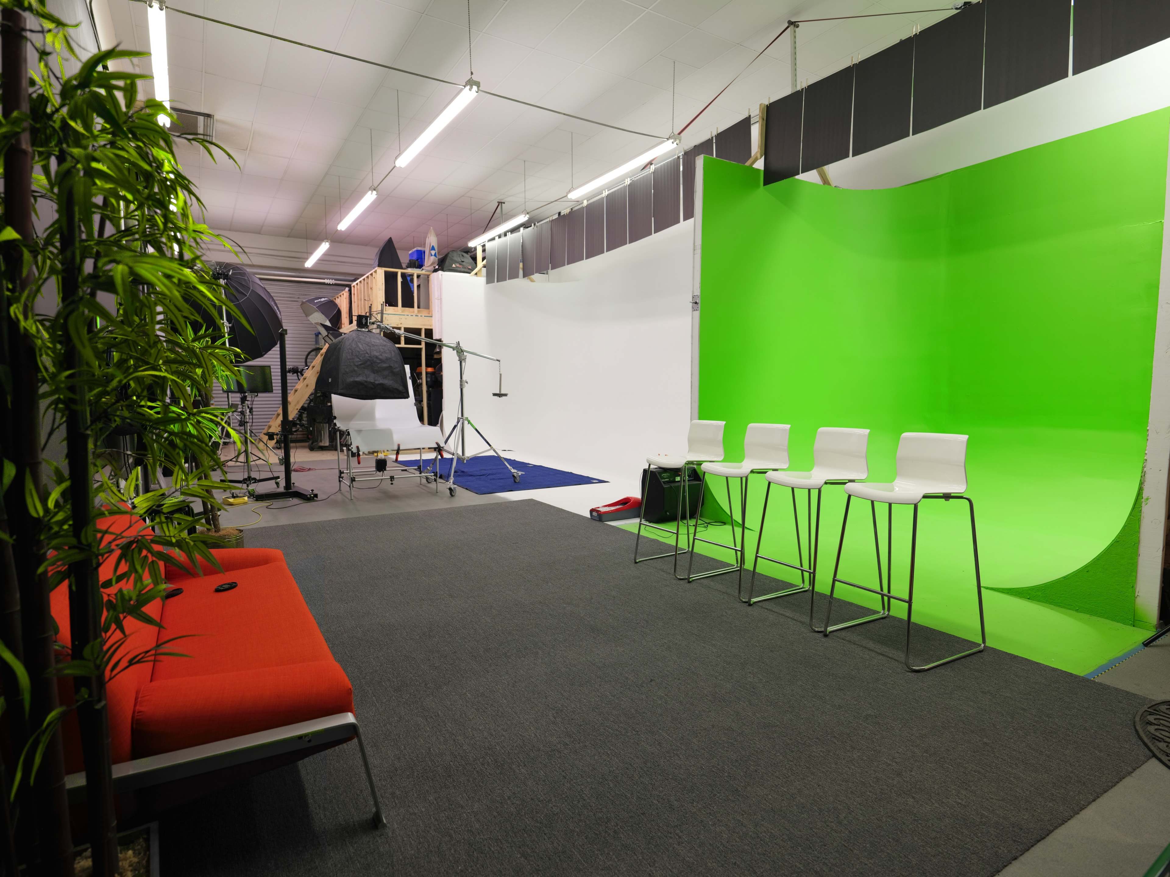 A photo studio with a green background, three white bar stools, and various photography equipment set up.