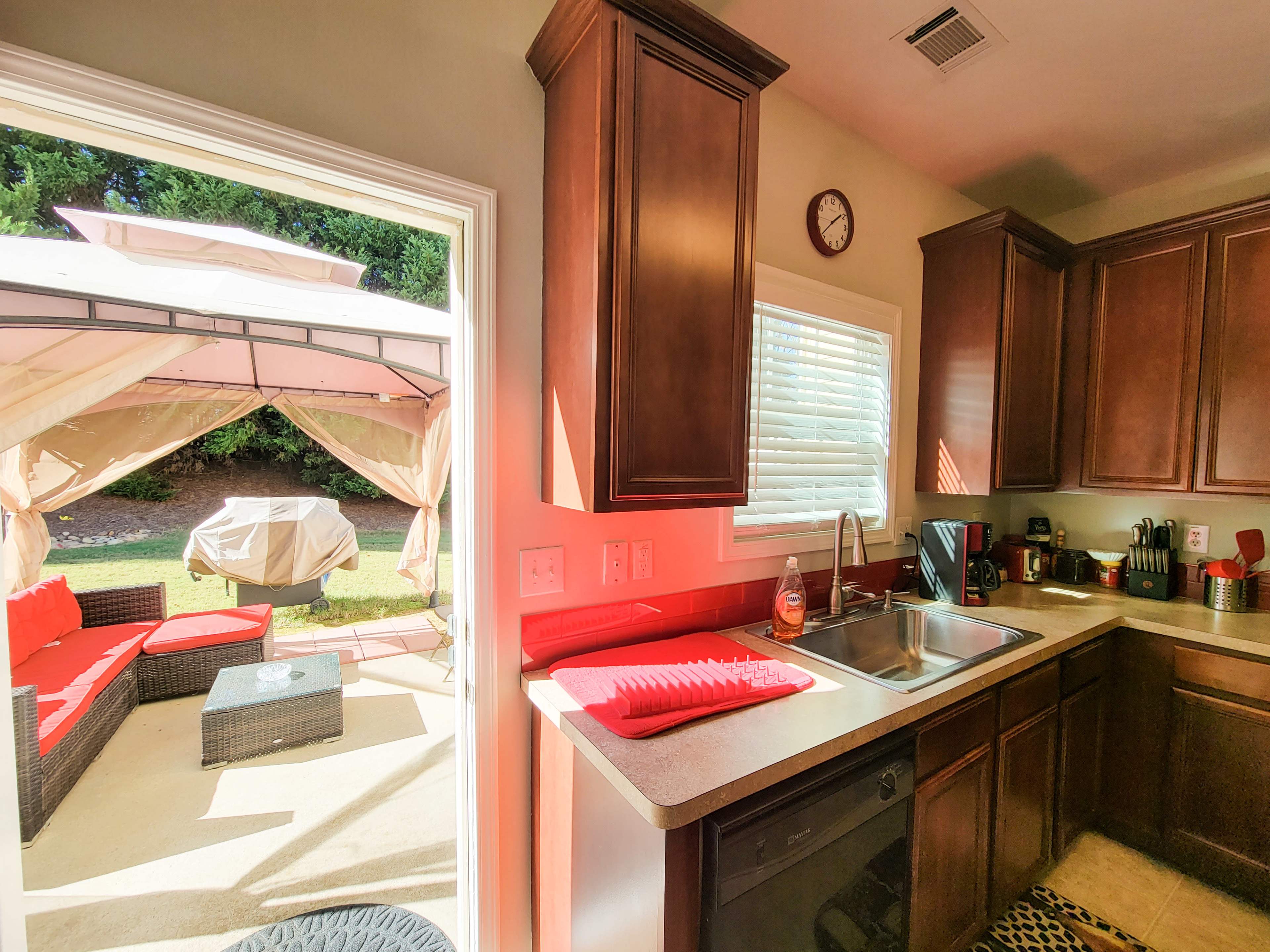 A kitchen with dark wood cabinets and a view of a patio featuring red furniture and a canopy.