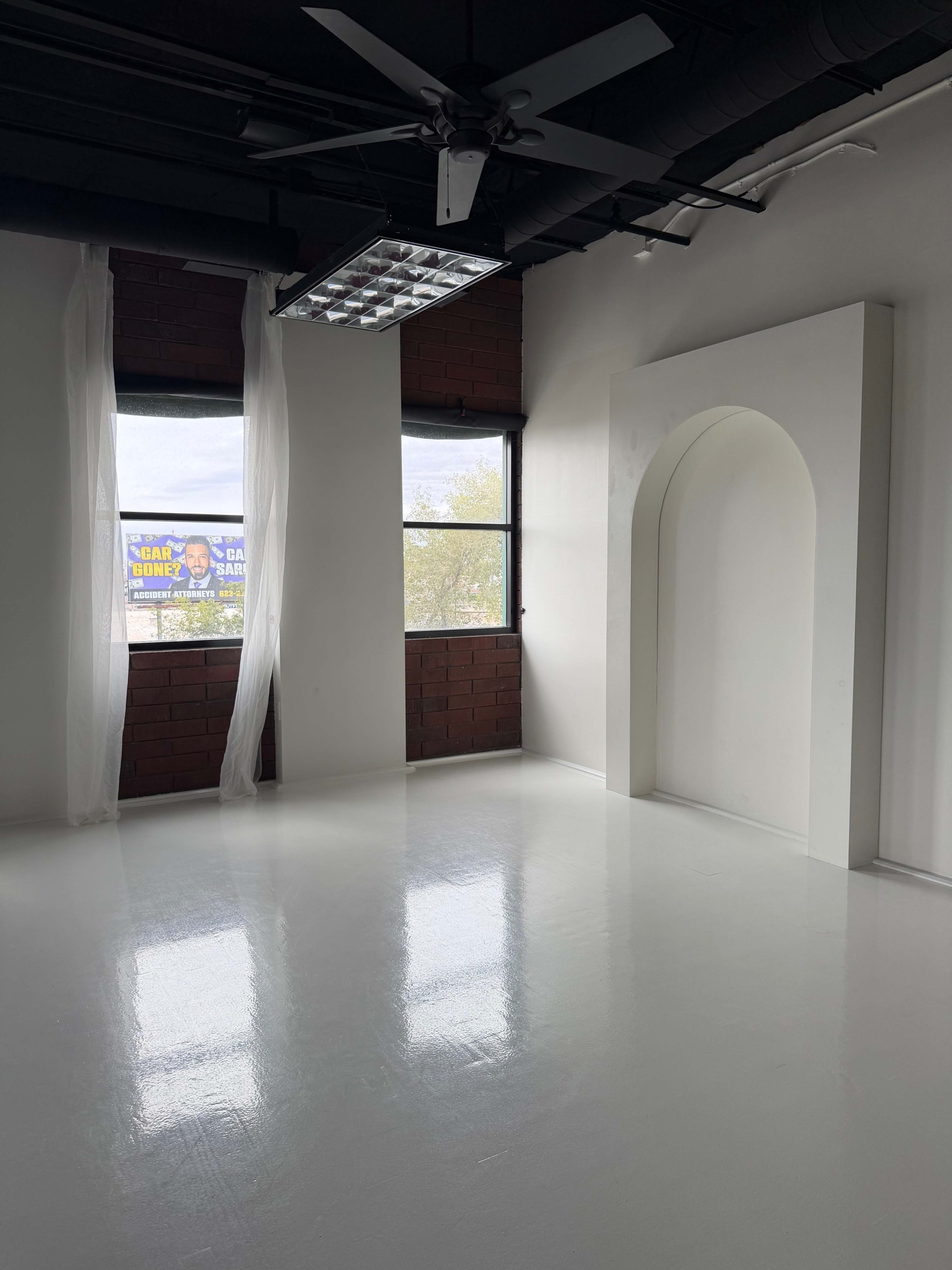 The image shows a minimalist room with a glossy white floor, large windows, and an arch-shaped architectural feature on the wall.