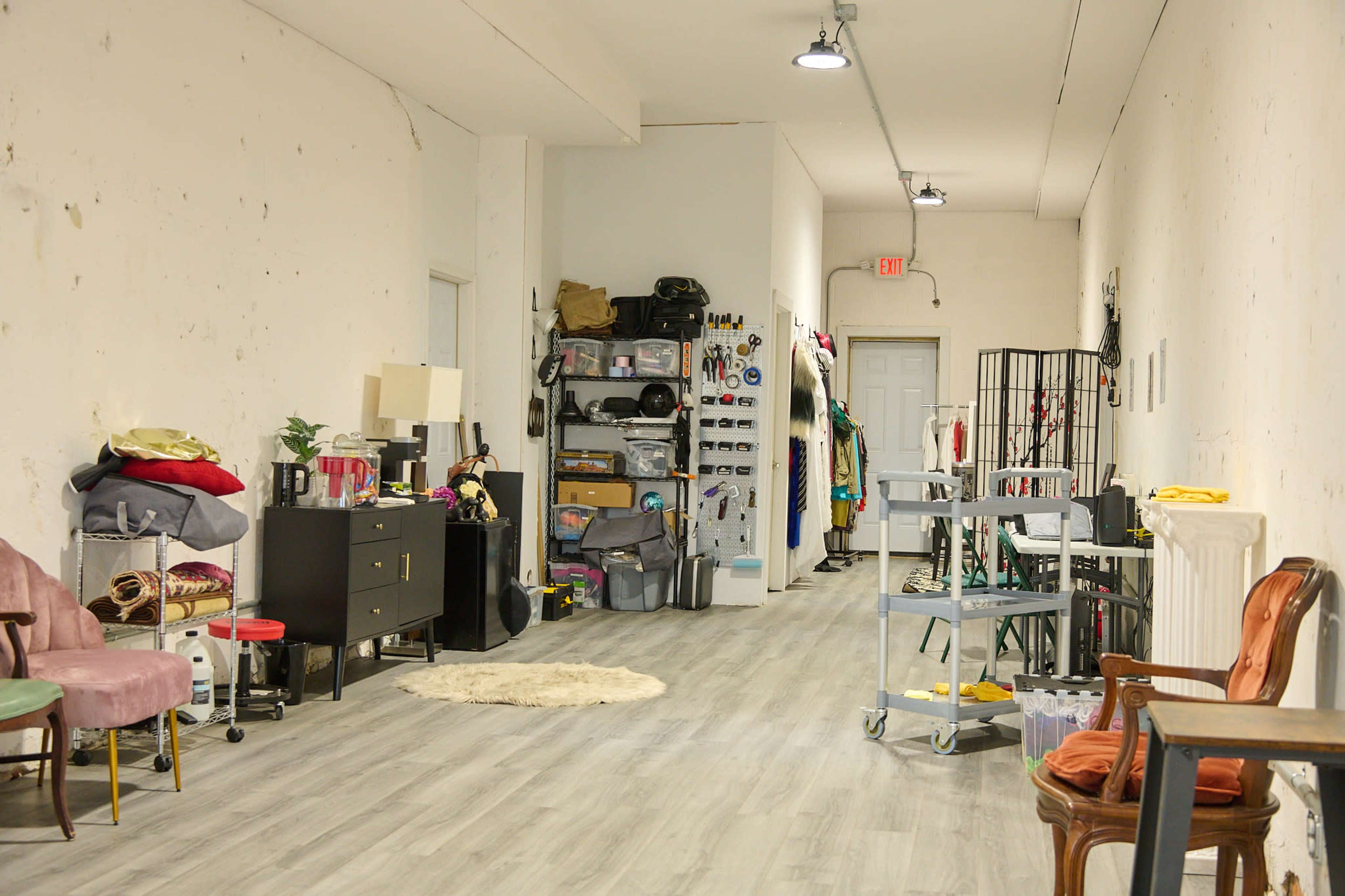 A long, narrow room featuring various furniture items, storage containers, and a section for hanging clothes along one wall.