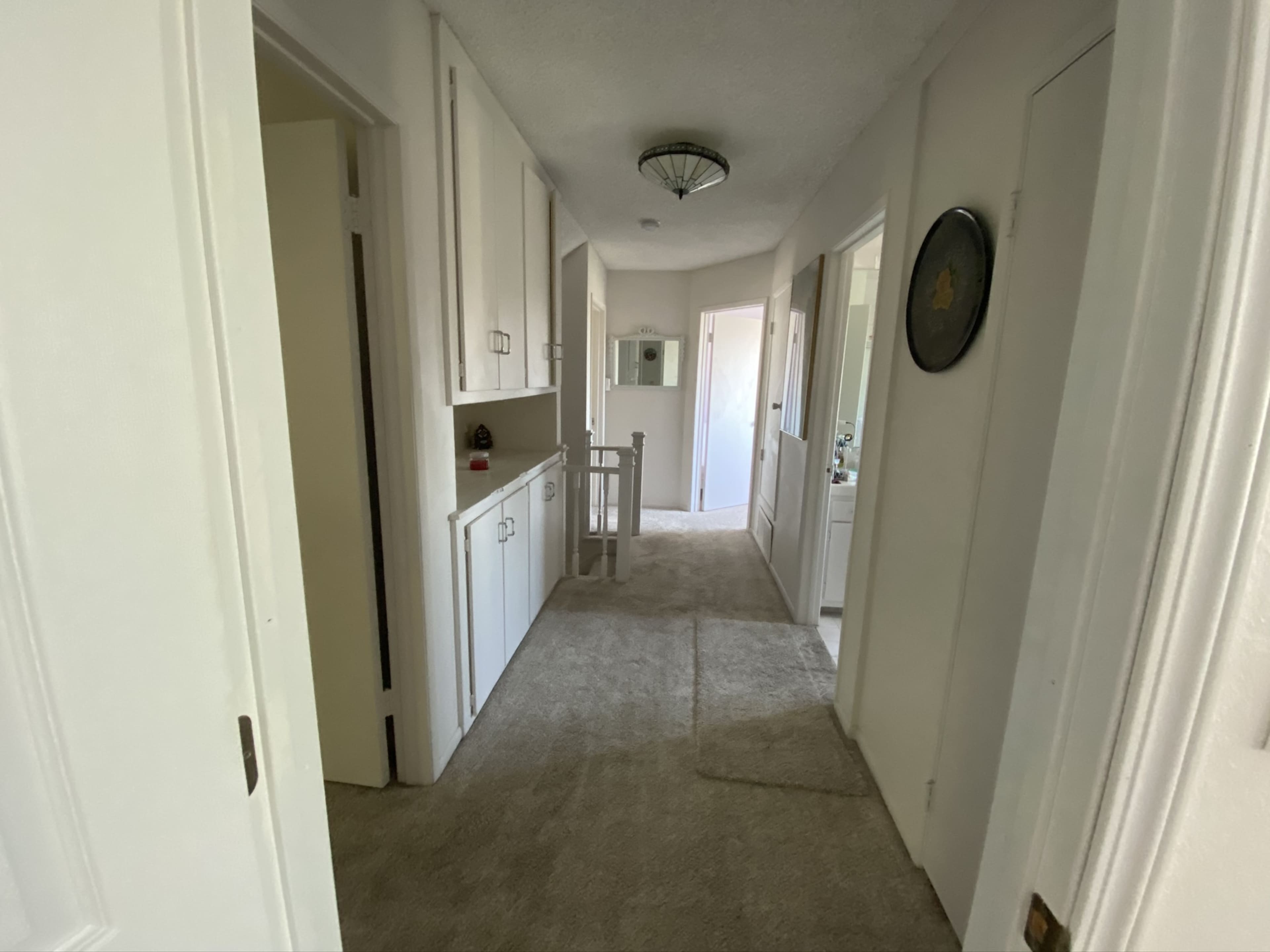 The image shows a hallway with light-colored walls, a carpeted floor, and several doors leading to adjacent rooms or areas.