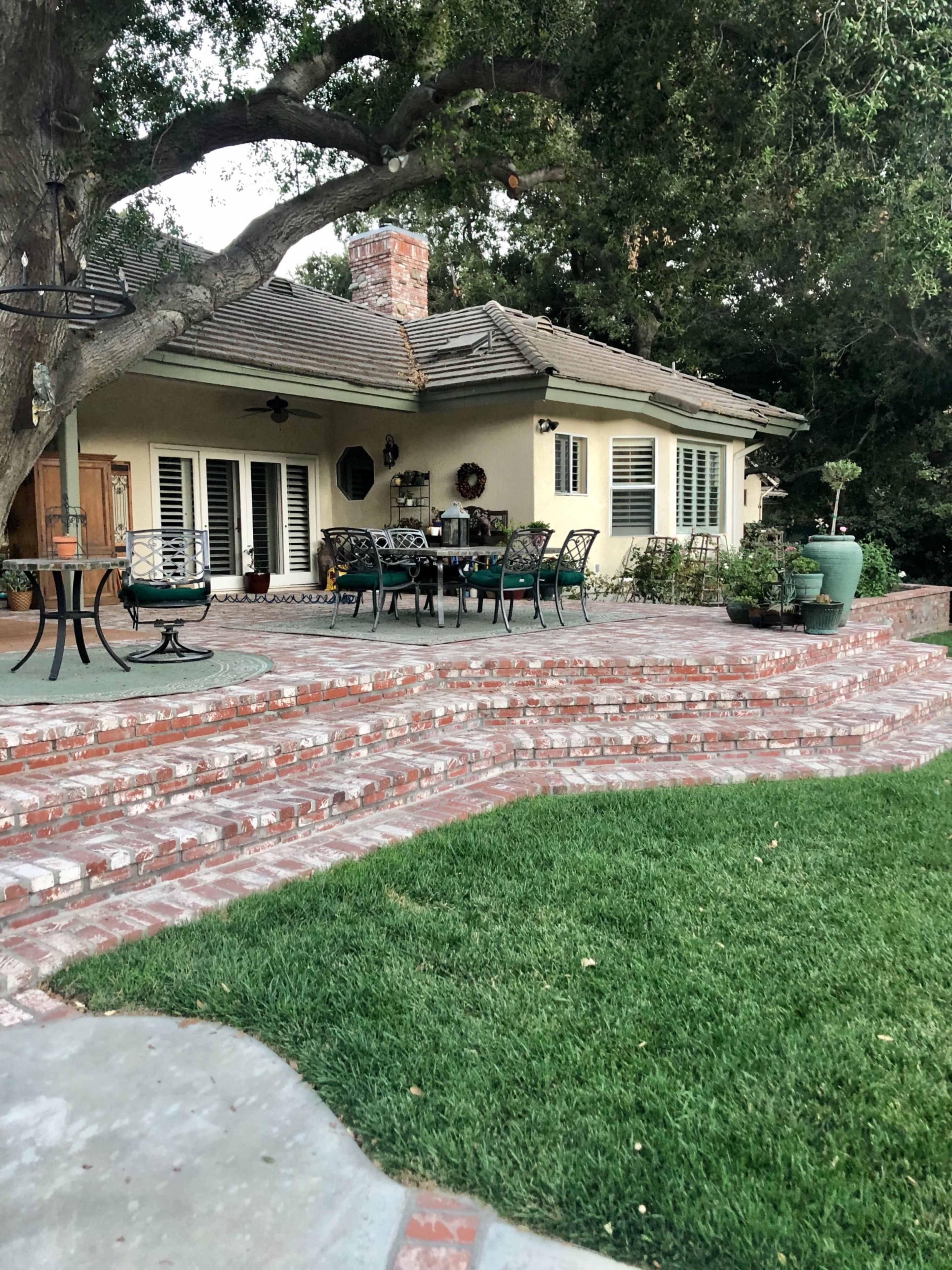 A patio area with brick steps leading up to a house surrounded by greenery and outdoor furniture.