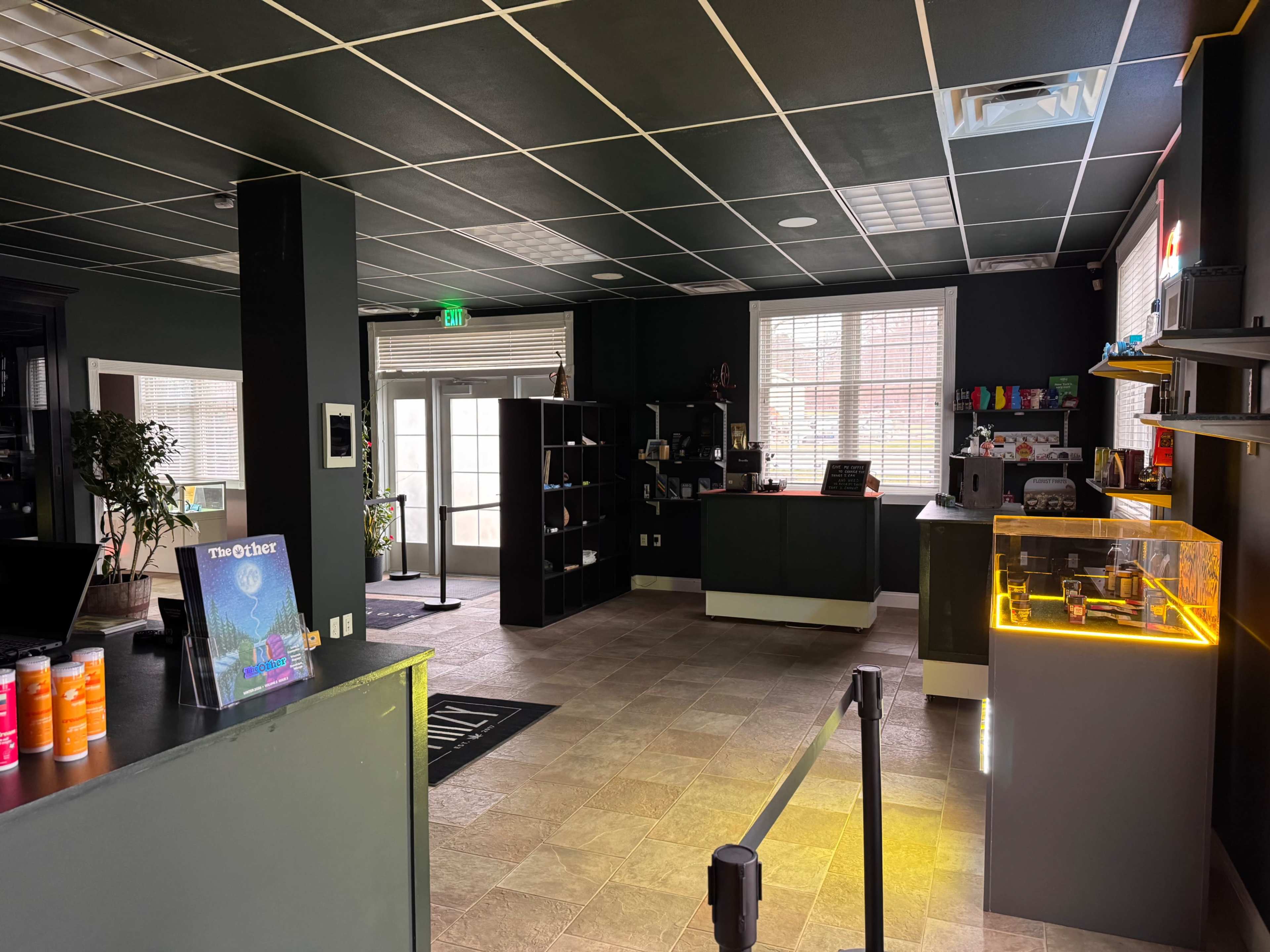 The image shows the interior of a modern retail space with a reception area, shelves displaying products, and a checkout counter.
