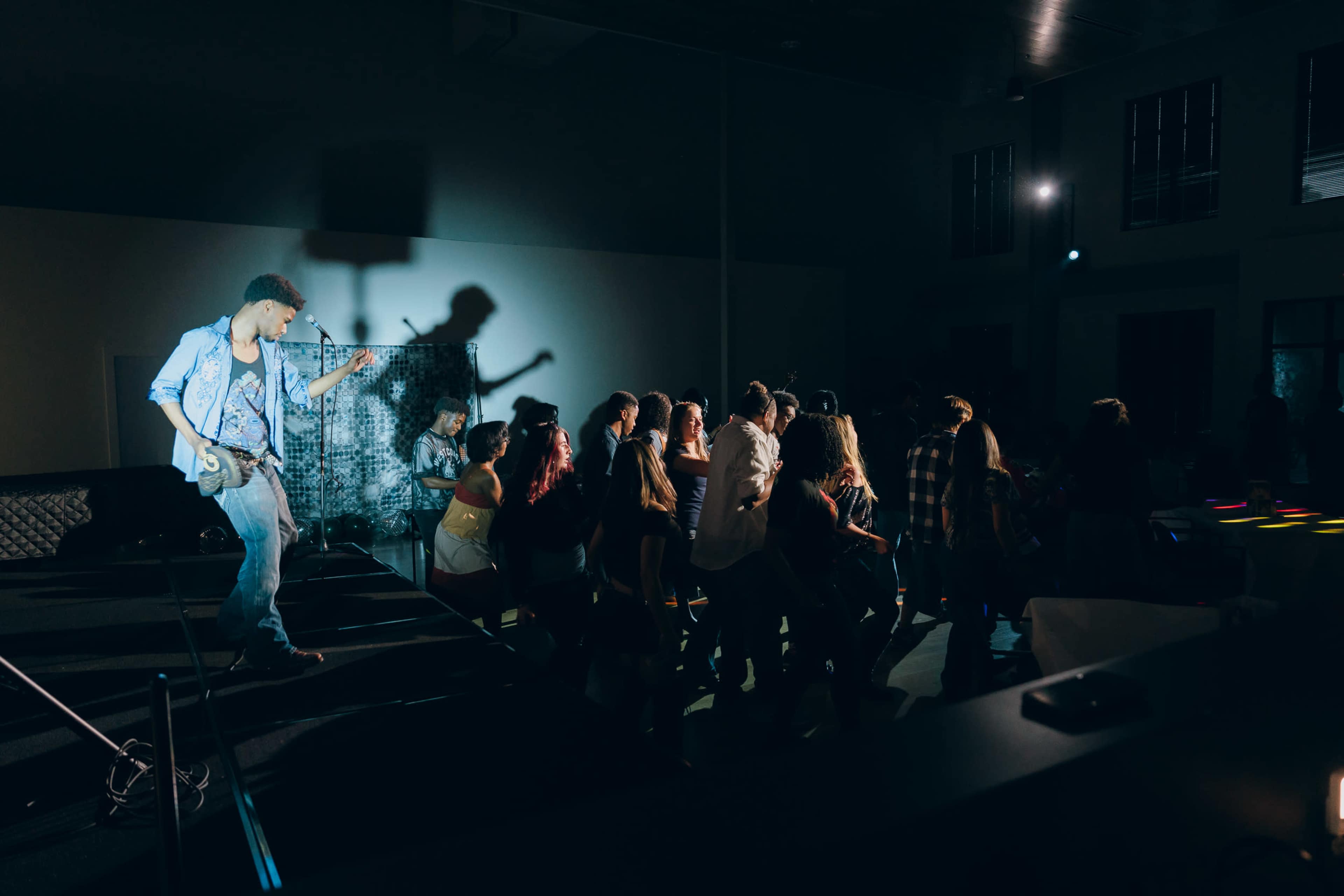 A musician performs on stage while a group of people dances in front of him at a lively event.