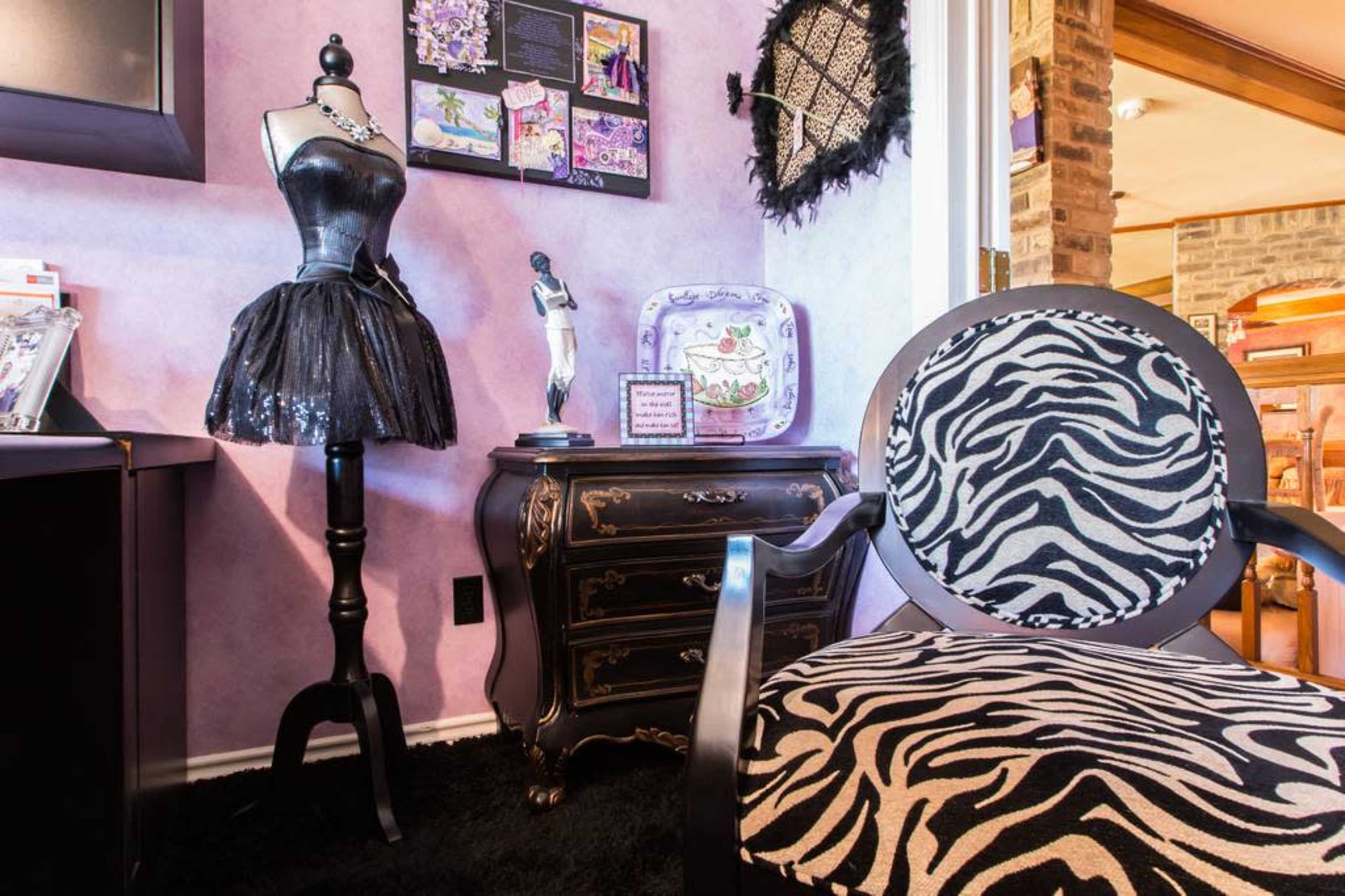 A room corner featuring a zebra-patterned chair, a dress form adorned with a black sequined dress, and a decorative chest of drawers against a purple wall.