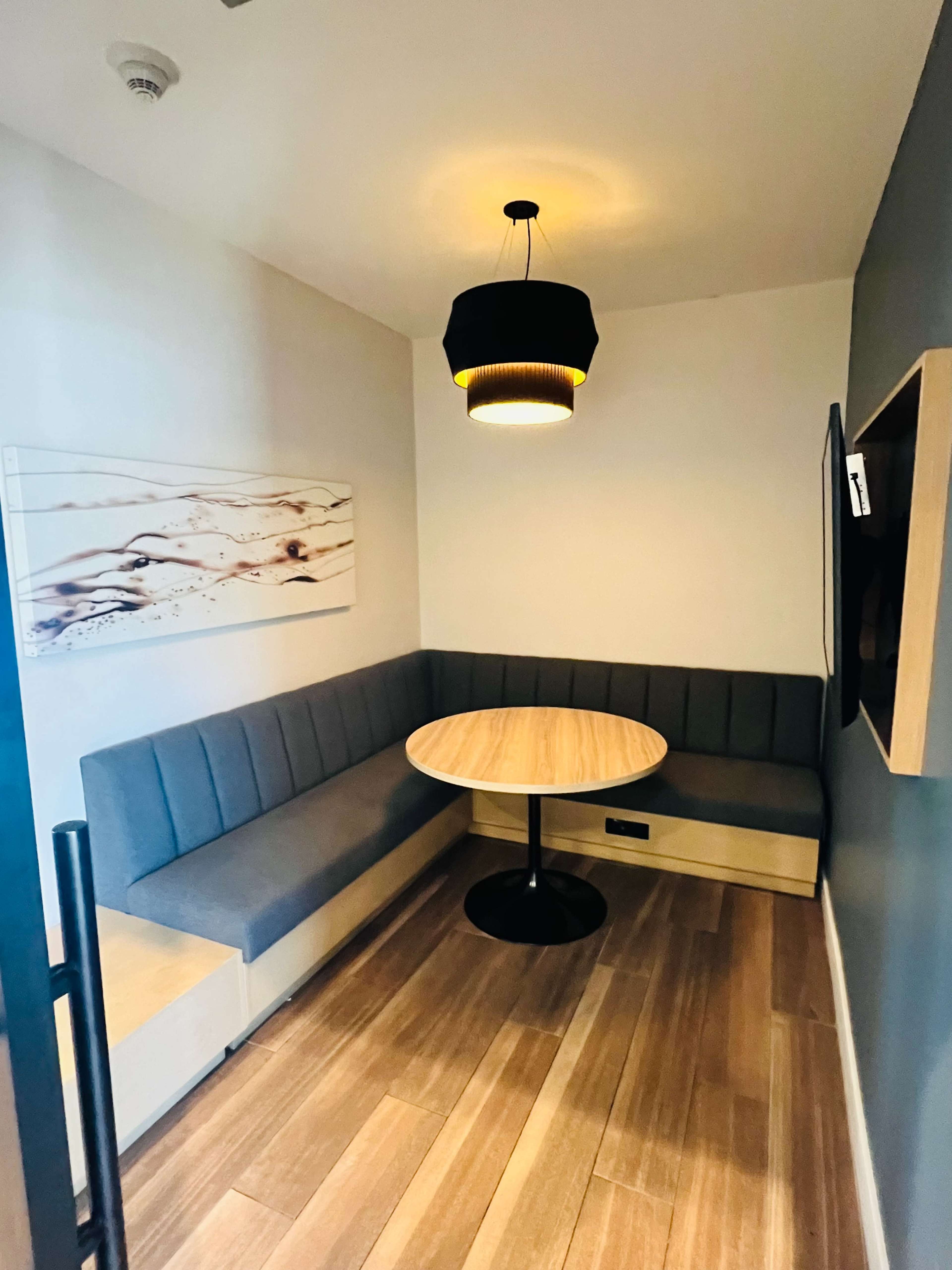 A small, modern seating area with a round table and a gray upholstered bench against the wall, illuminated by a pendant light.