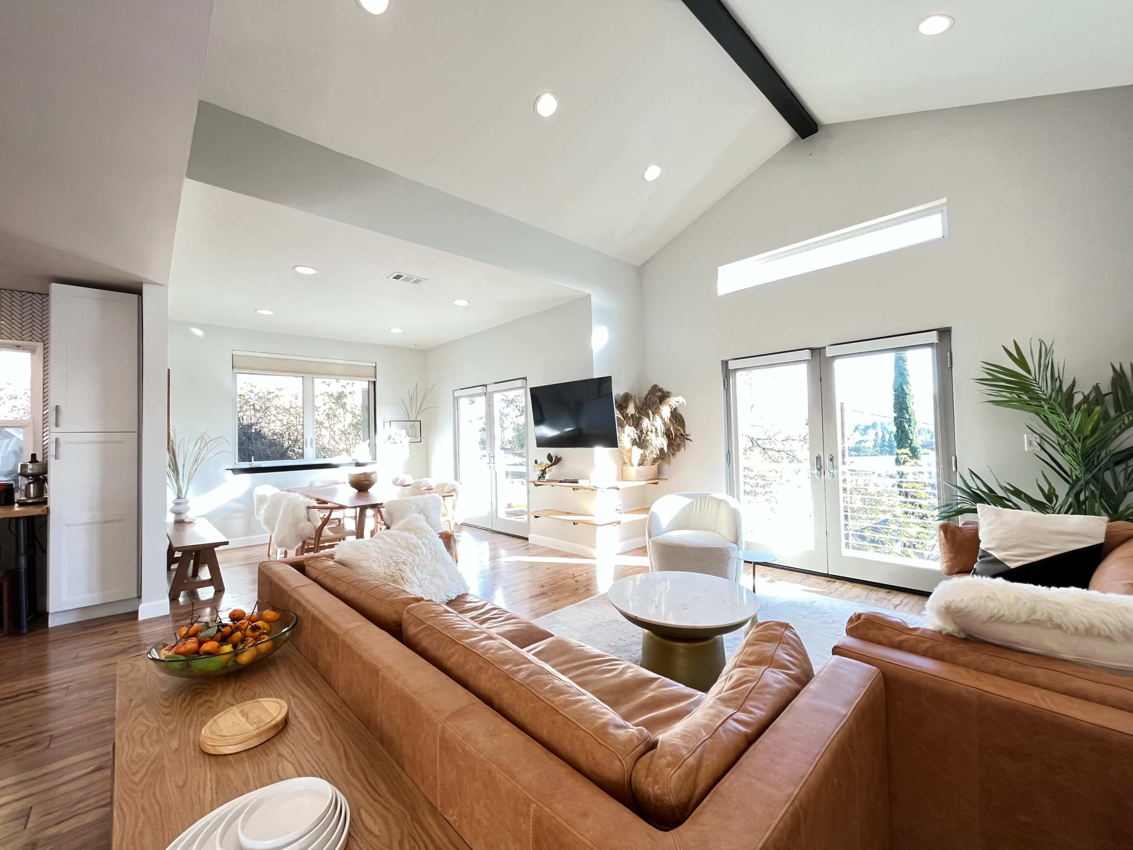 A modern, open-concept living room with a leather sofa, wooden furniture, and large windows that provide ample natural light.