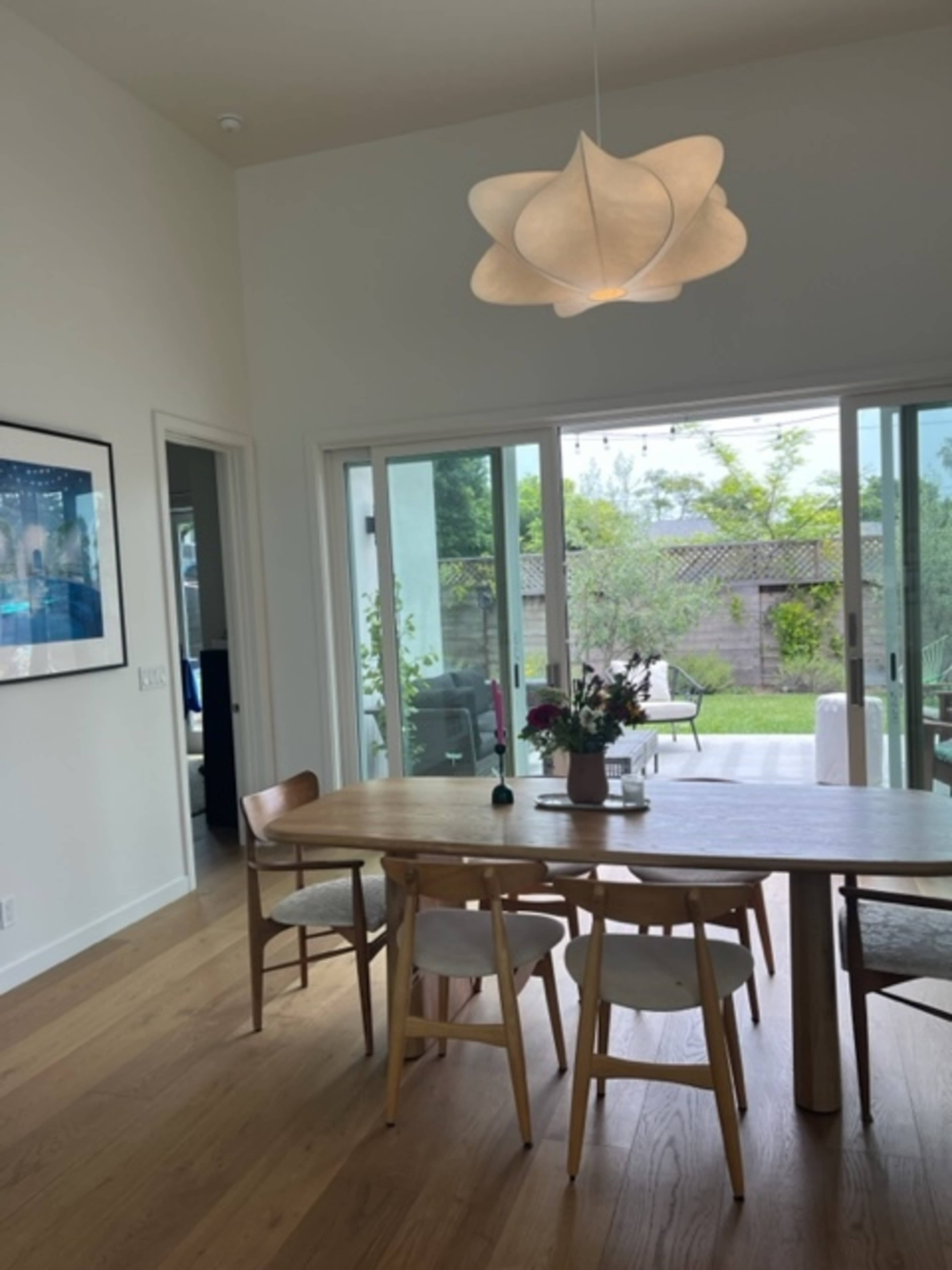 A dining area features a wooden table with six chairs and a large window overlooking a garden.
