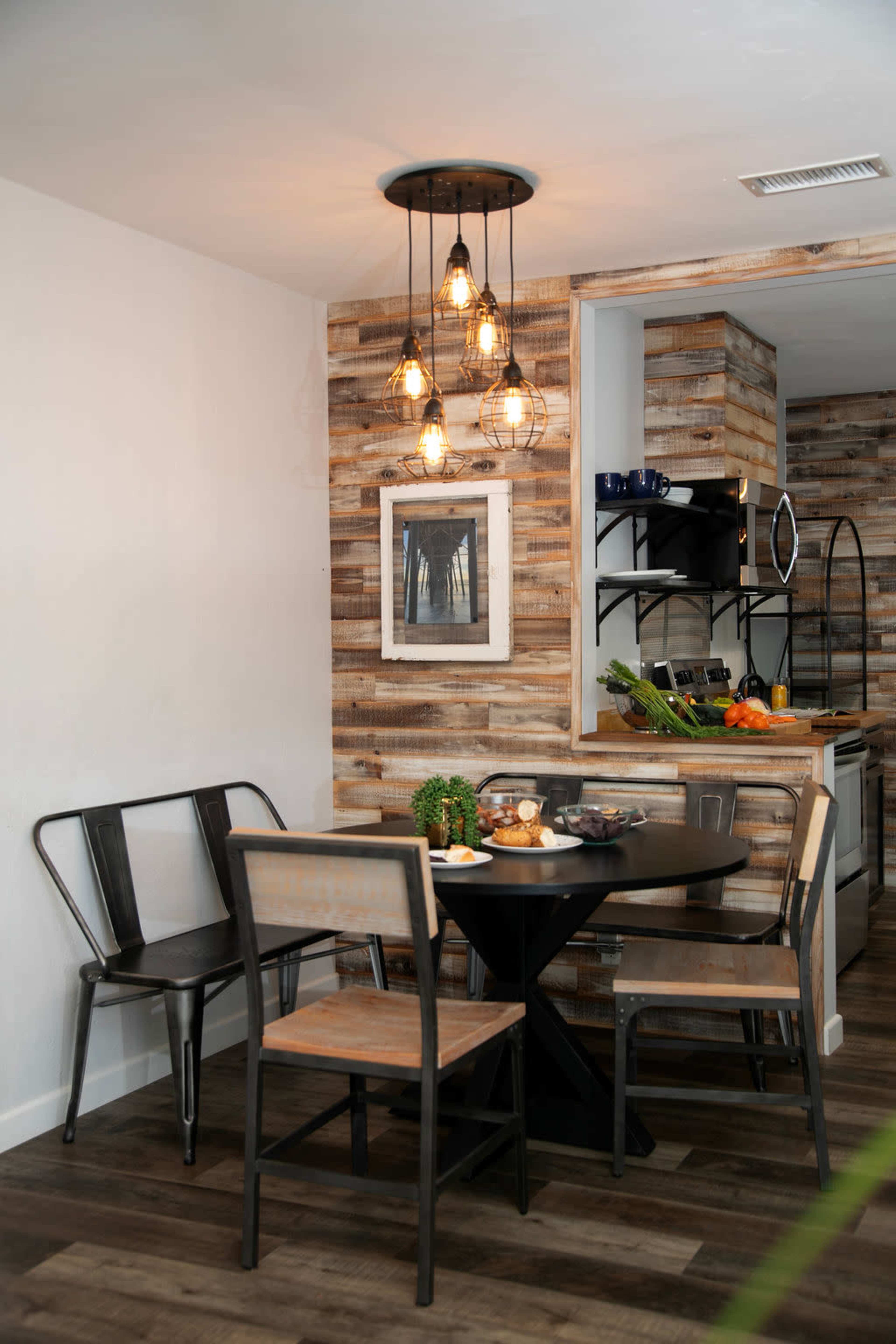 A small dining area features a round black table surrounded by four chairs, with a wooden accent wall and hanging light fixtures.