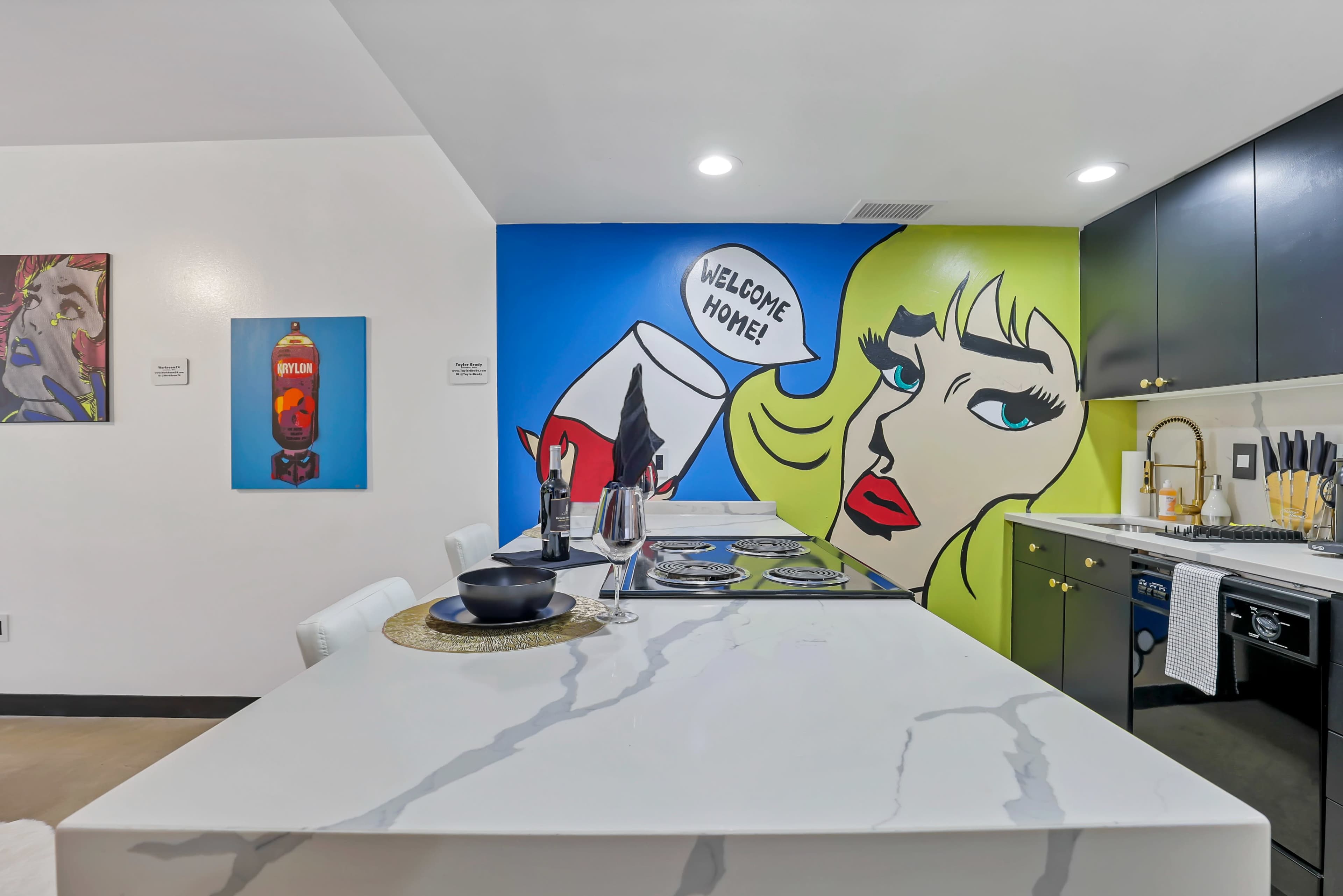 The kitchen features a marble island, a colorful mural on the wall, and modern black cabinetry.